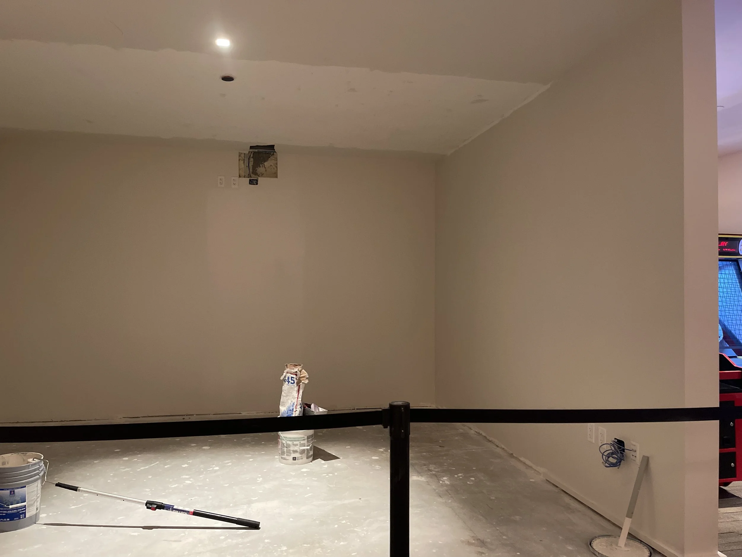 Room under renovation with construction materials including a bucket, paint, and tools on the floor, with unfinished walls and ceiling.