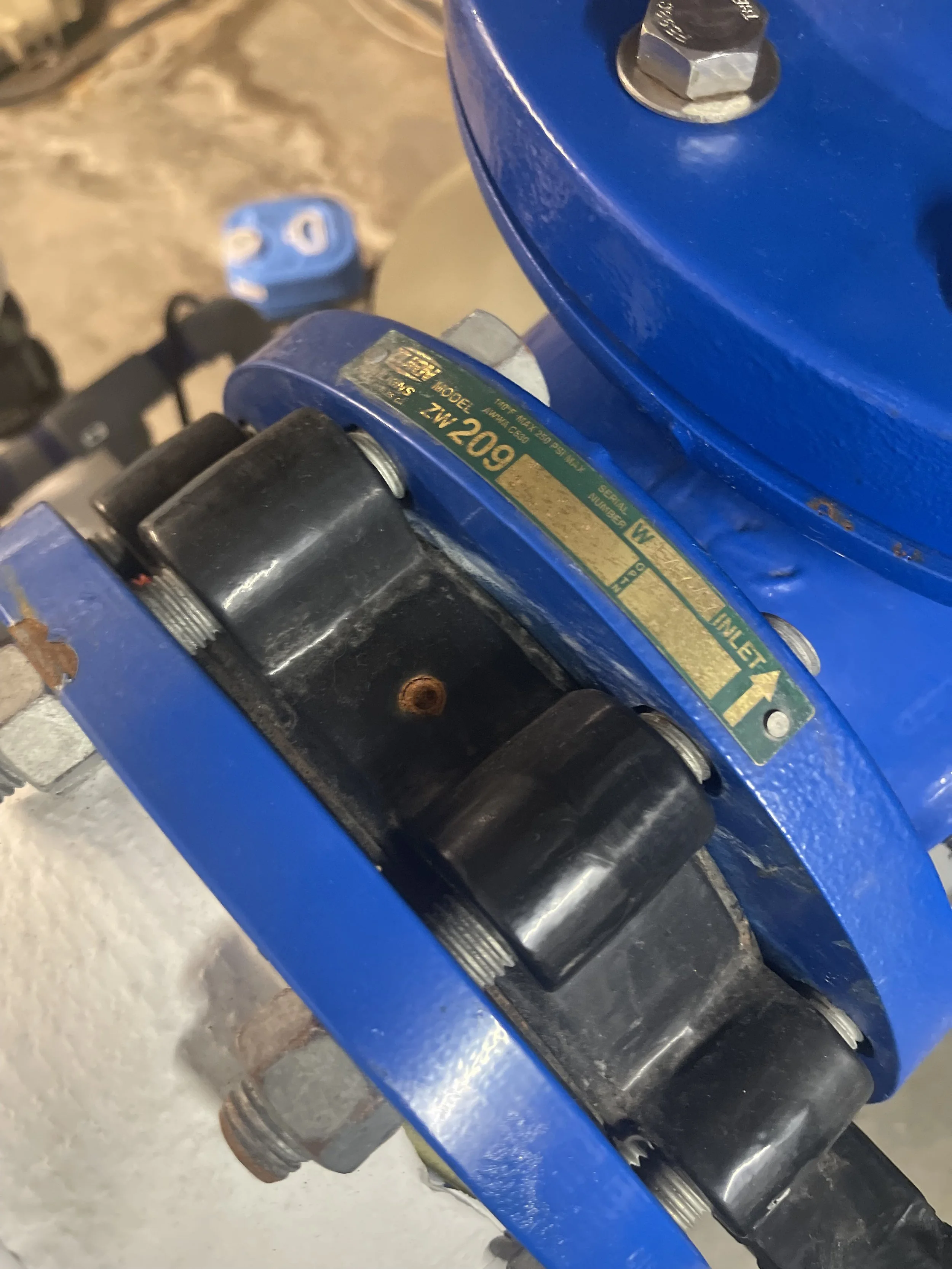 Close-up view of a blue industrial valve with black rollers and a gold label indicating model and specifications.