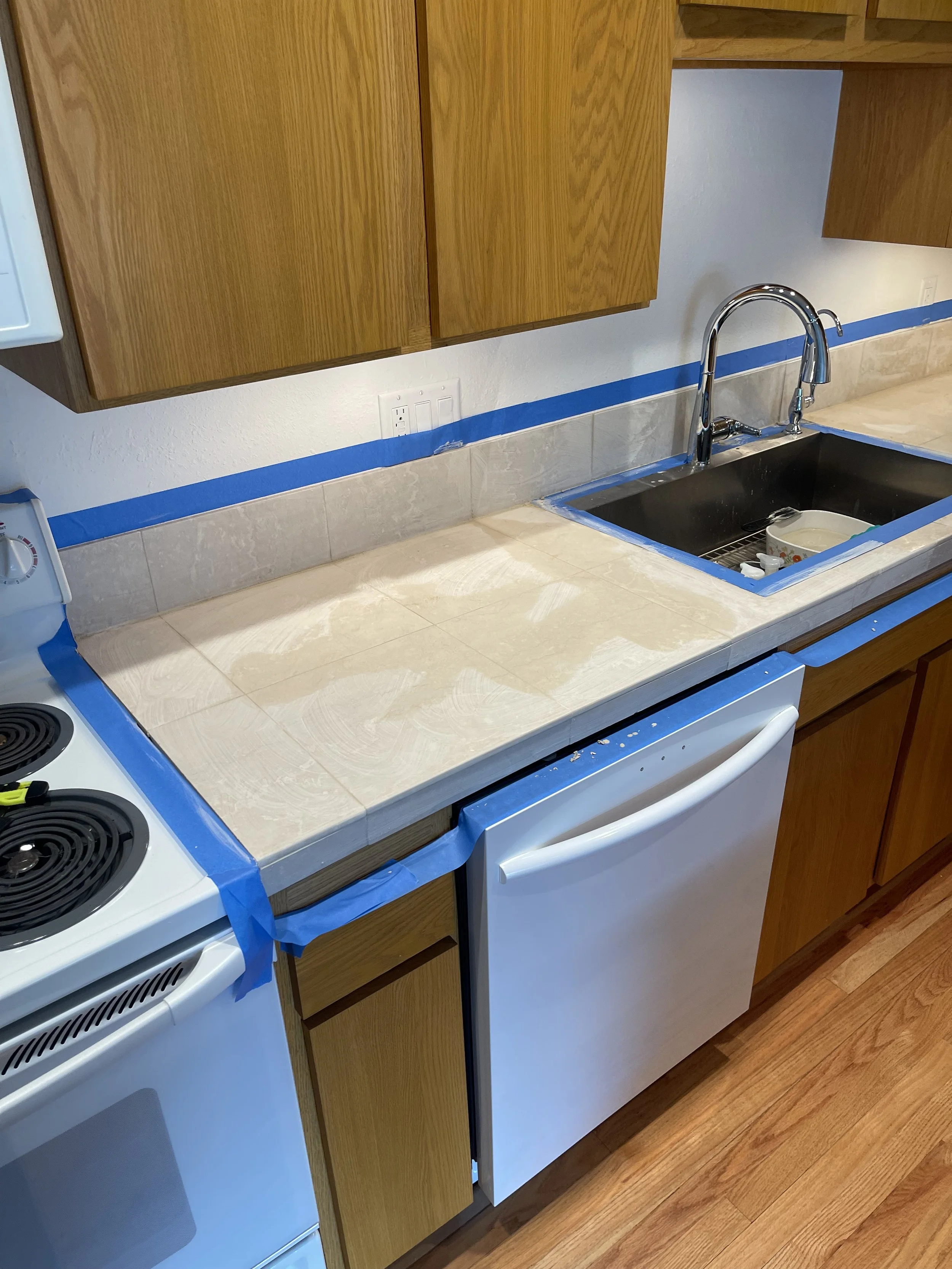 Kitchen countertop with masking tape applied around stove, sink, and edges, in preparation for tile installation.