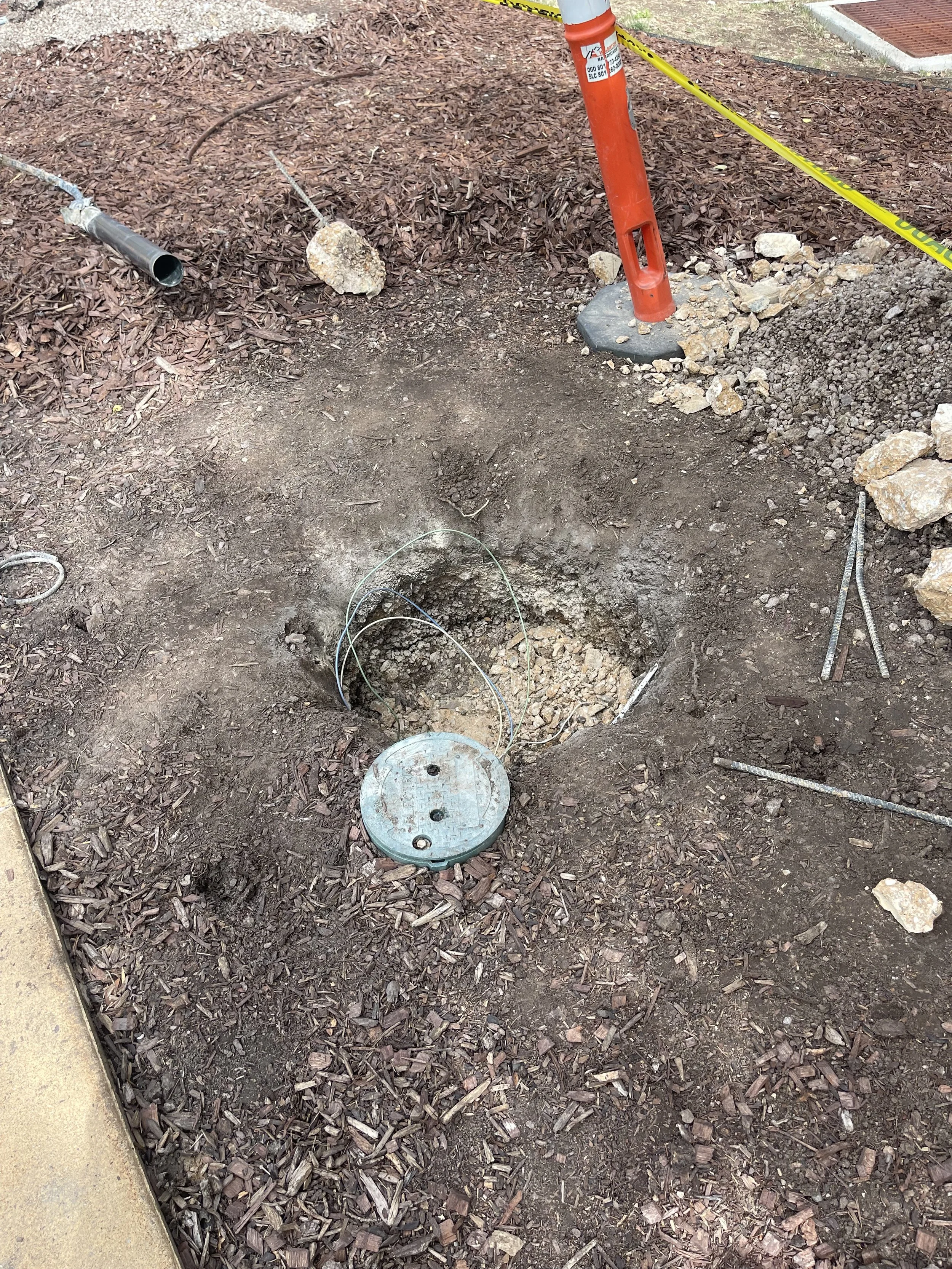 Construction site with a hole in the ground, safety barrier, and utility access cover