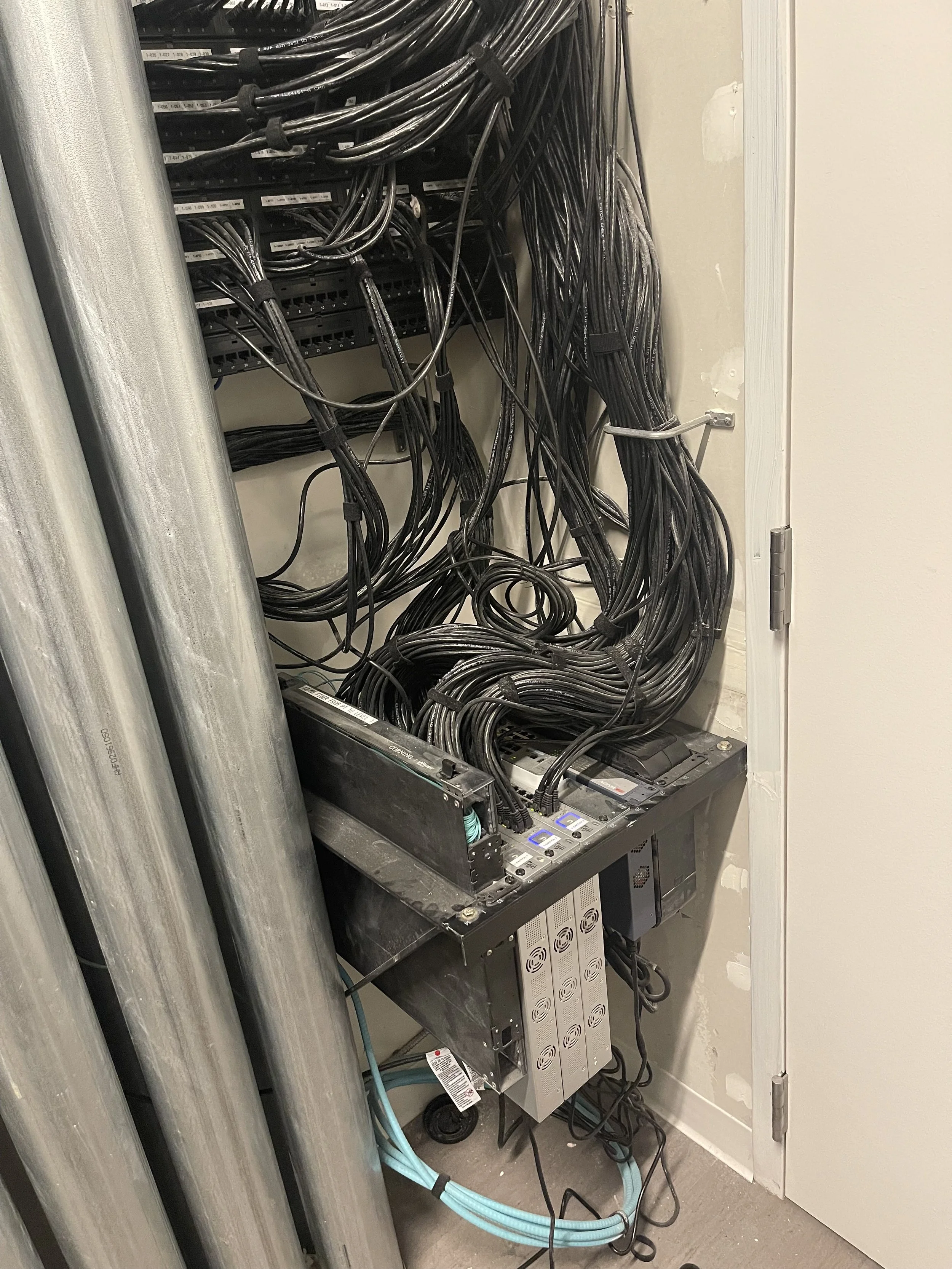 Server rack with tangled black cables inside a utility closet.