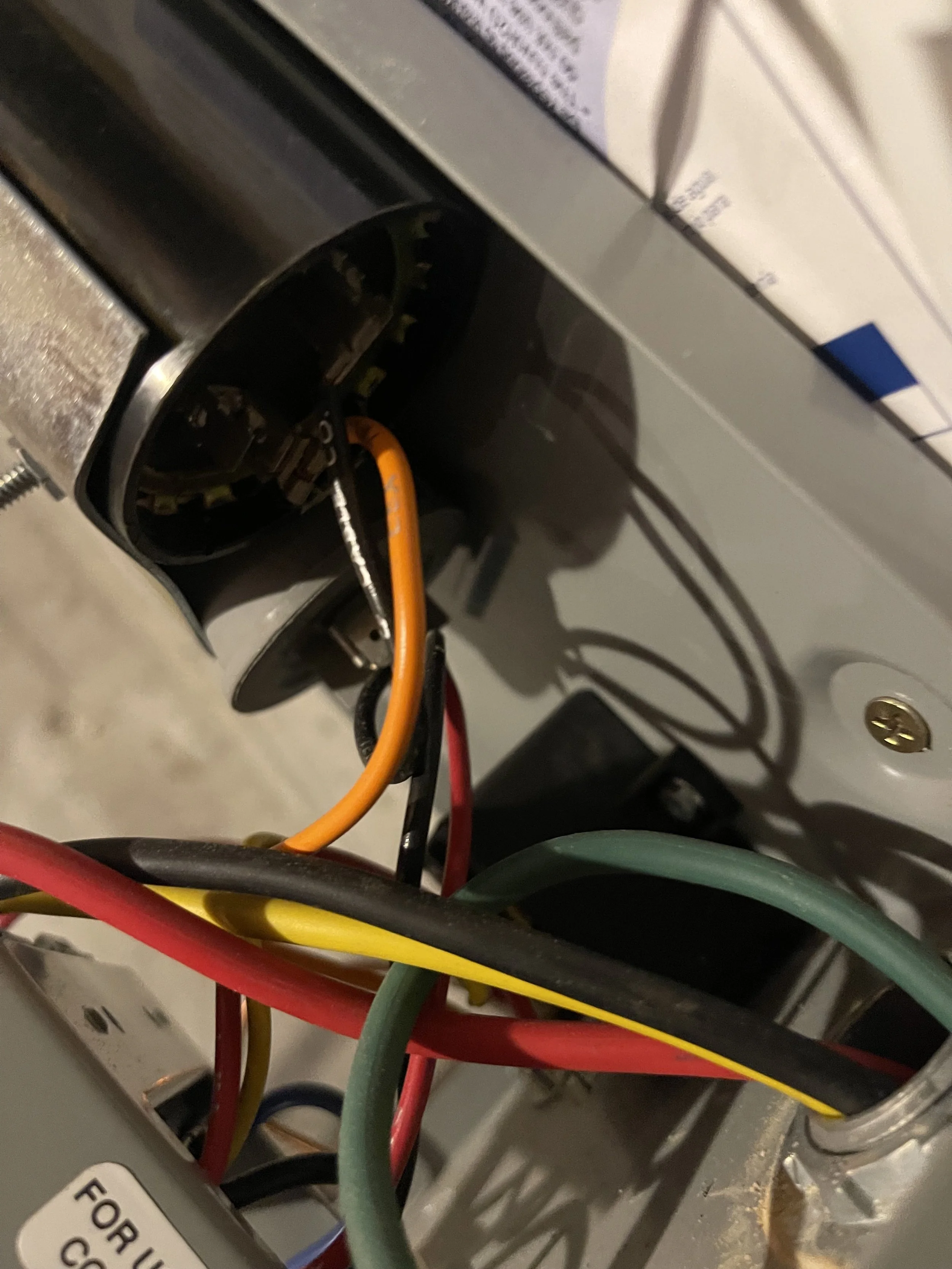 Close-up of electrical wires inside an electronic device or appliance, with a metallic circular component and a printed circuit board partially visible.