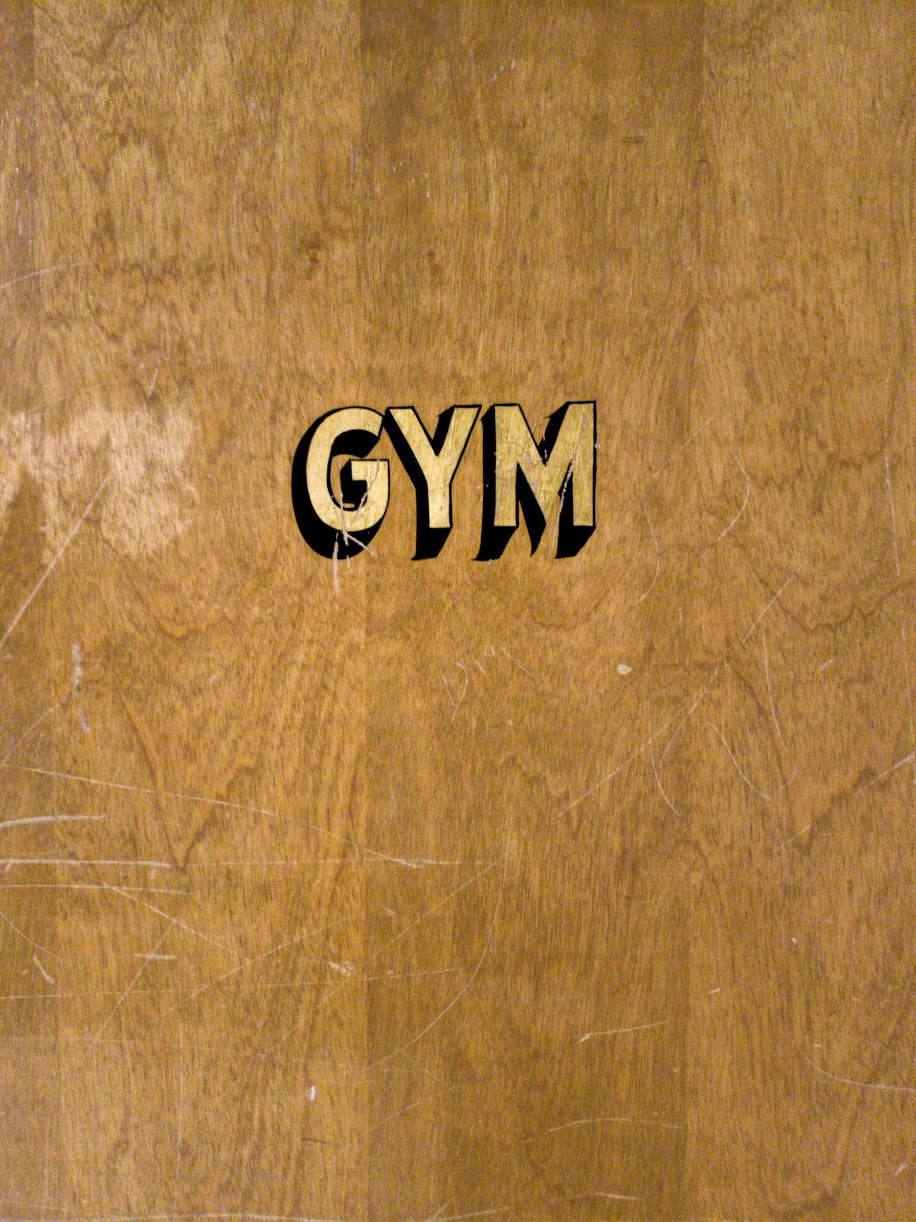 A wooden gym door with the word 'GYM' written in bold black and tan letters.
