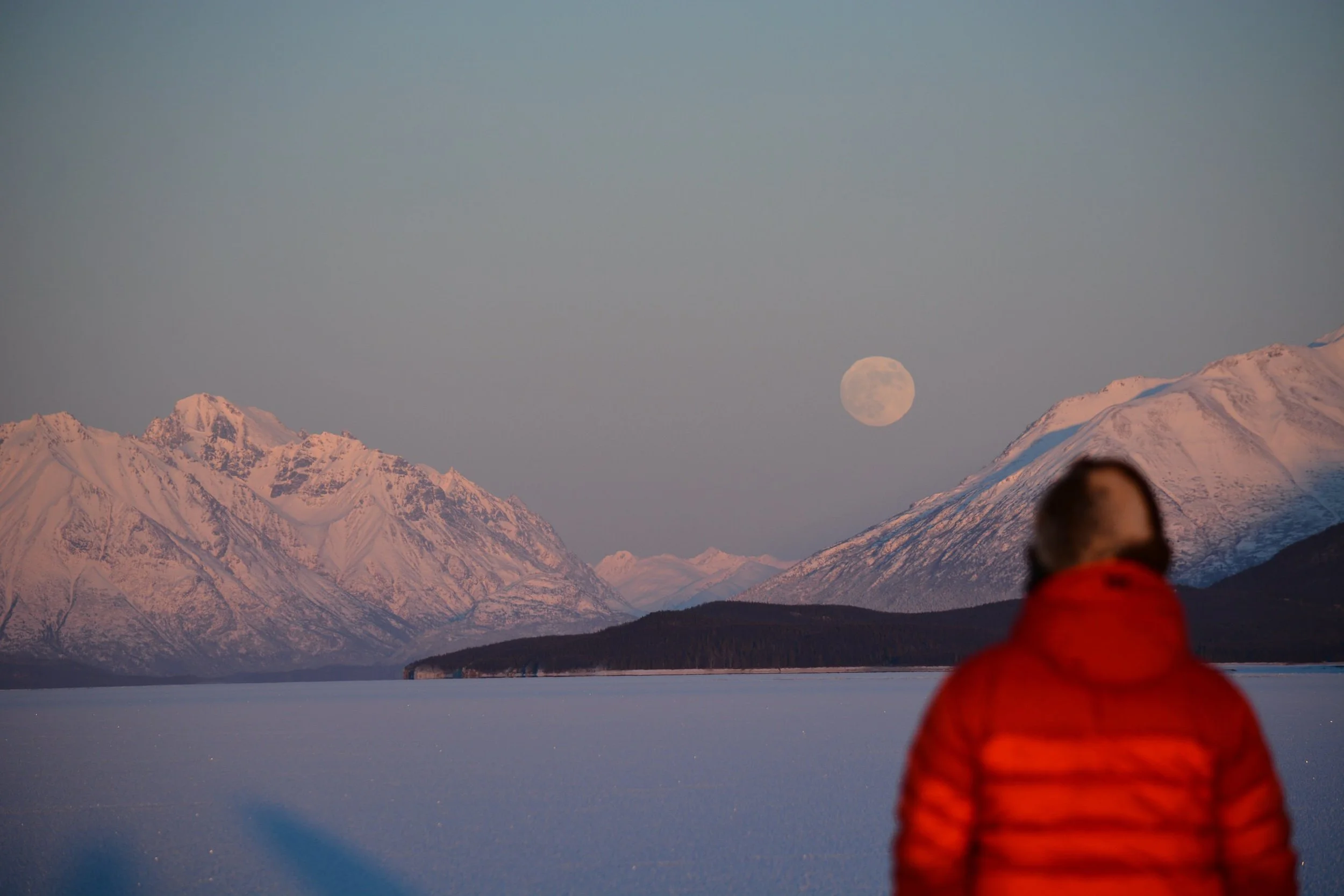 Person watching the full moon rise over frozen Lake Clark