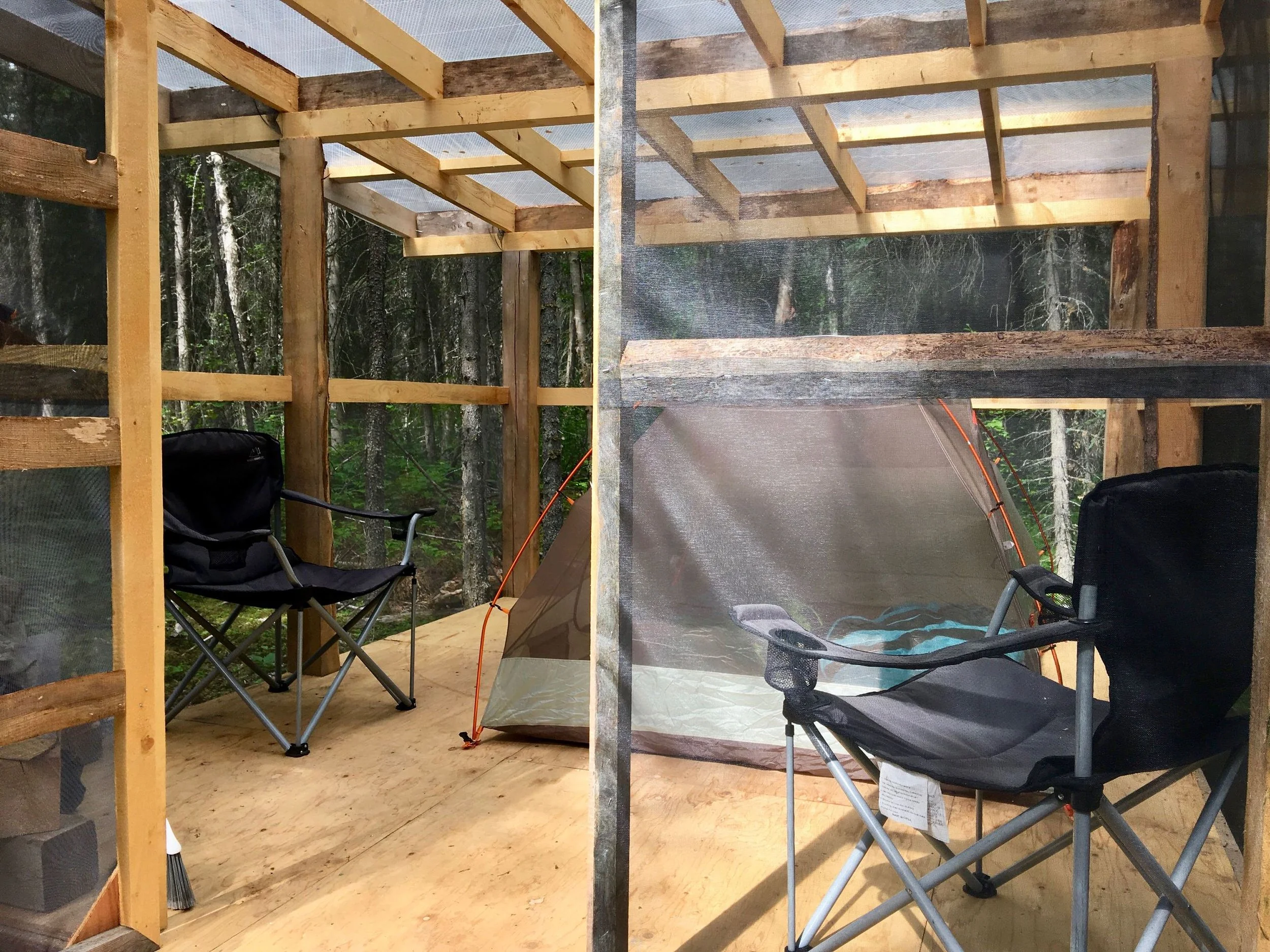 Port Alsworth campground hut with a Marmot Tungsten 3 person tent set up inside and 2 x-large camp chairs with a table.
