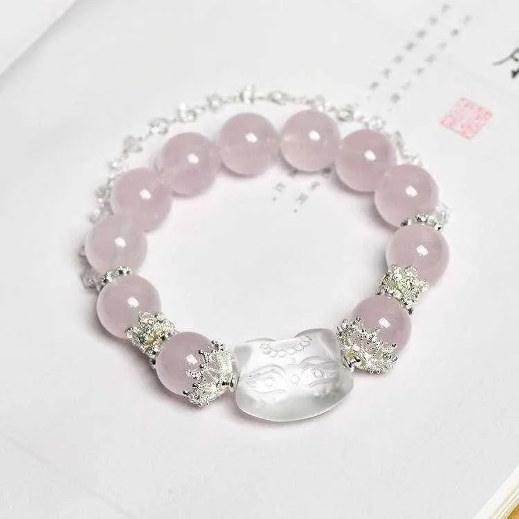 Pink beaded bracelet with a clear carved stone centerpiece and silver spacer beads with rhinestones, displayed on white paper. Natural clear, and pink quartz bracelet with a cat design gemstone.