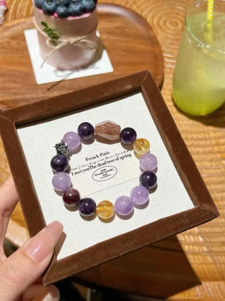 A beaded bracelet with purple, yellow, red, and dark purple beads inside a wooden box, with a note inside that reads, "French Paris. I met you. Amethyst, Black Obsidian: Protection, grounding, psychic shielding and Smoky Quartz.