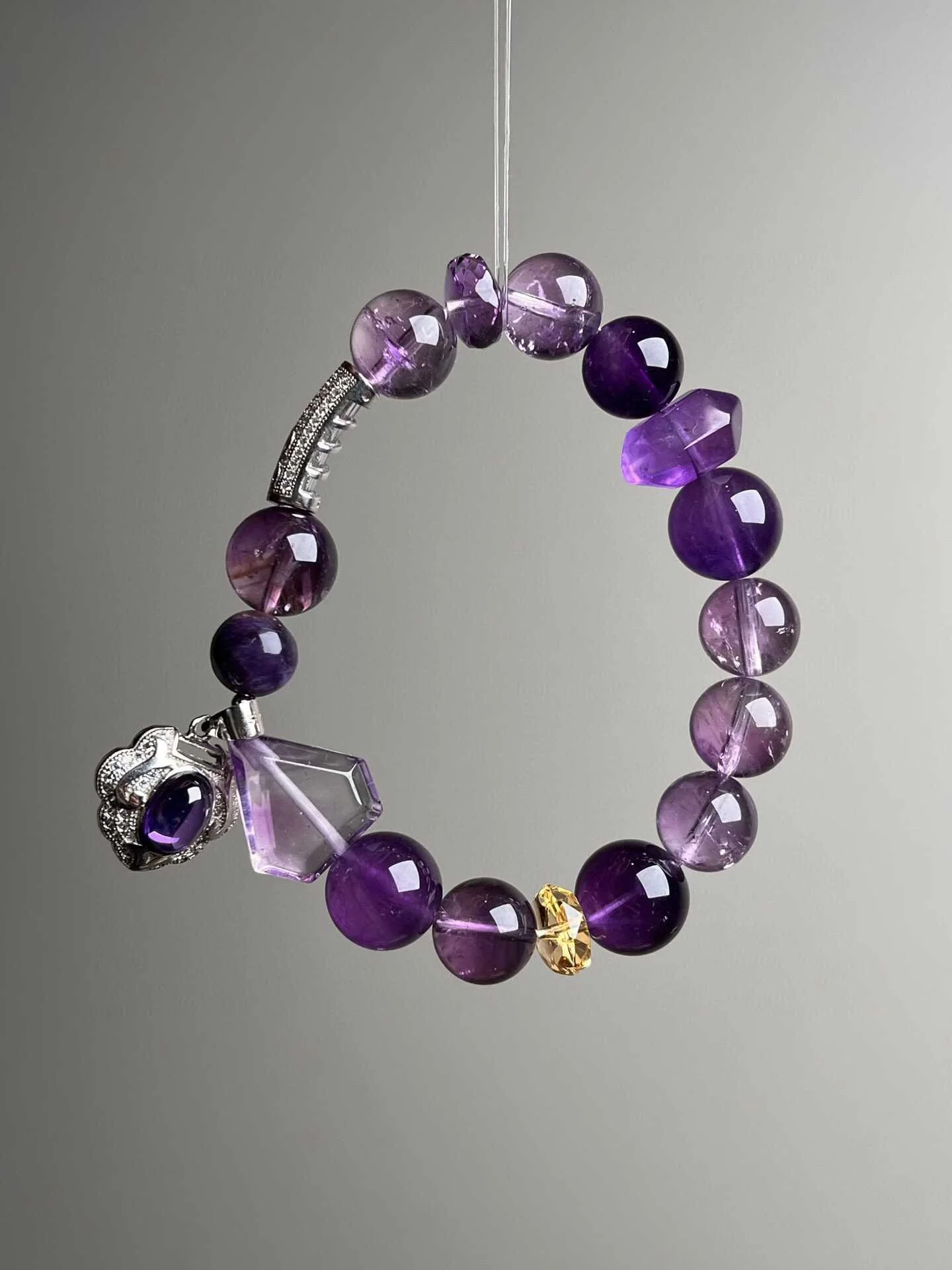 A bracelet made of natural crystals, purple and lilac beads, featuring a large purple gemstone pendant, with a small yellow bead and a decorative silver element—Amethyst, Black Obsidian: Protection, grounding, psychic shielding. Clear Quartz