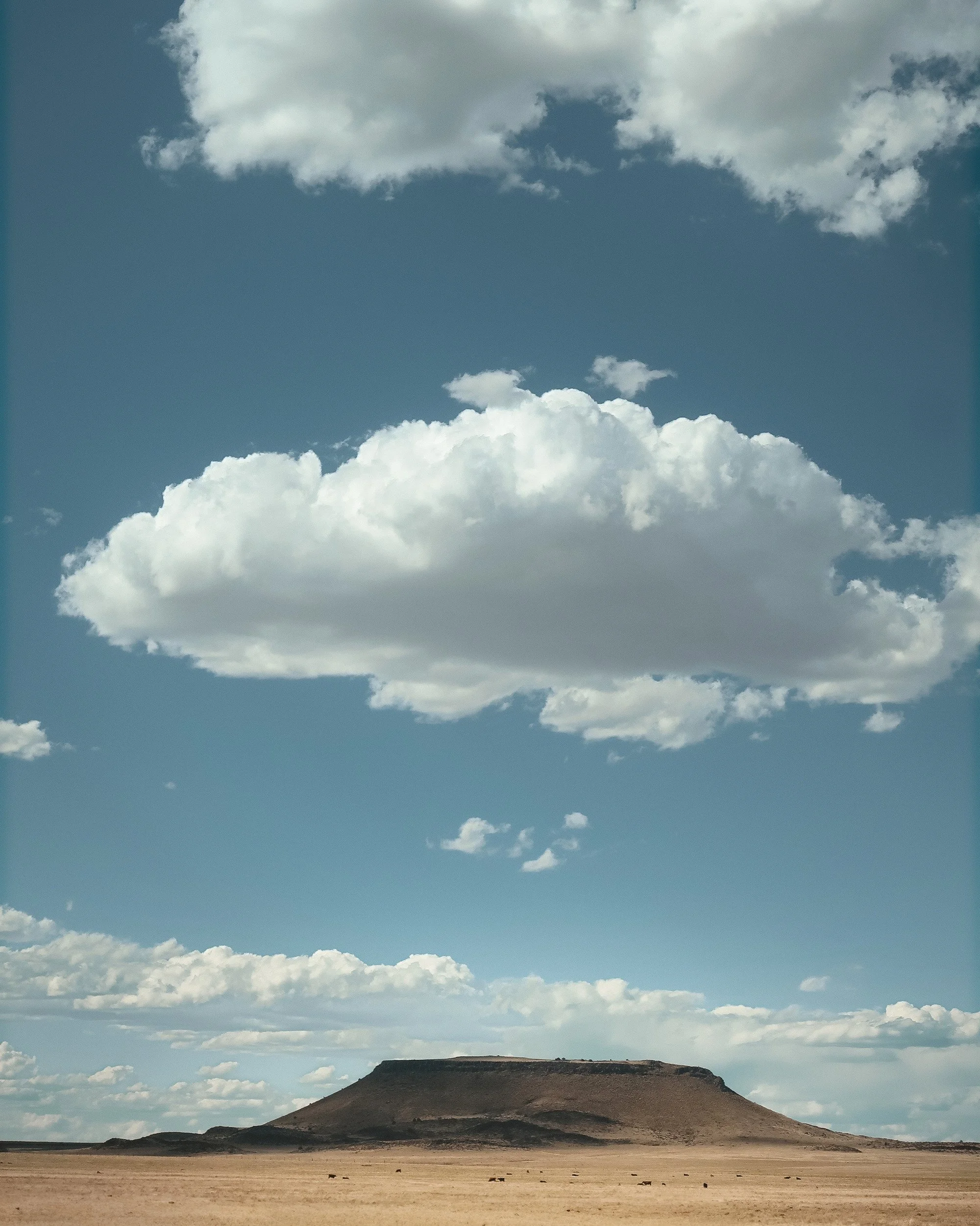 A lone flat-topped mesa on the West Texas plain under a tall blue sky, one white cloud floating high above it.