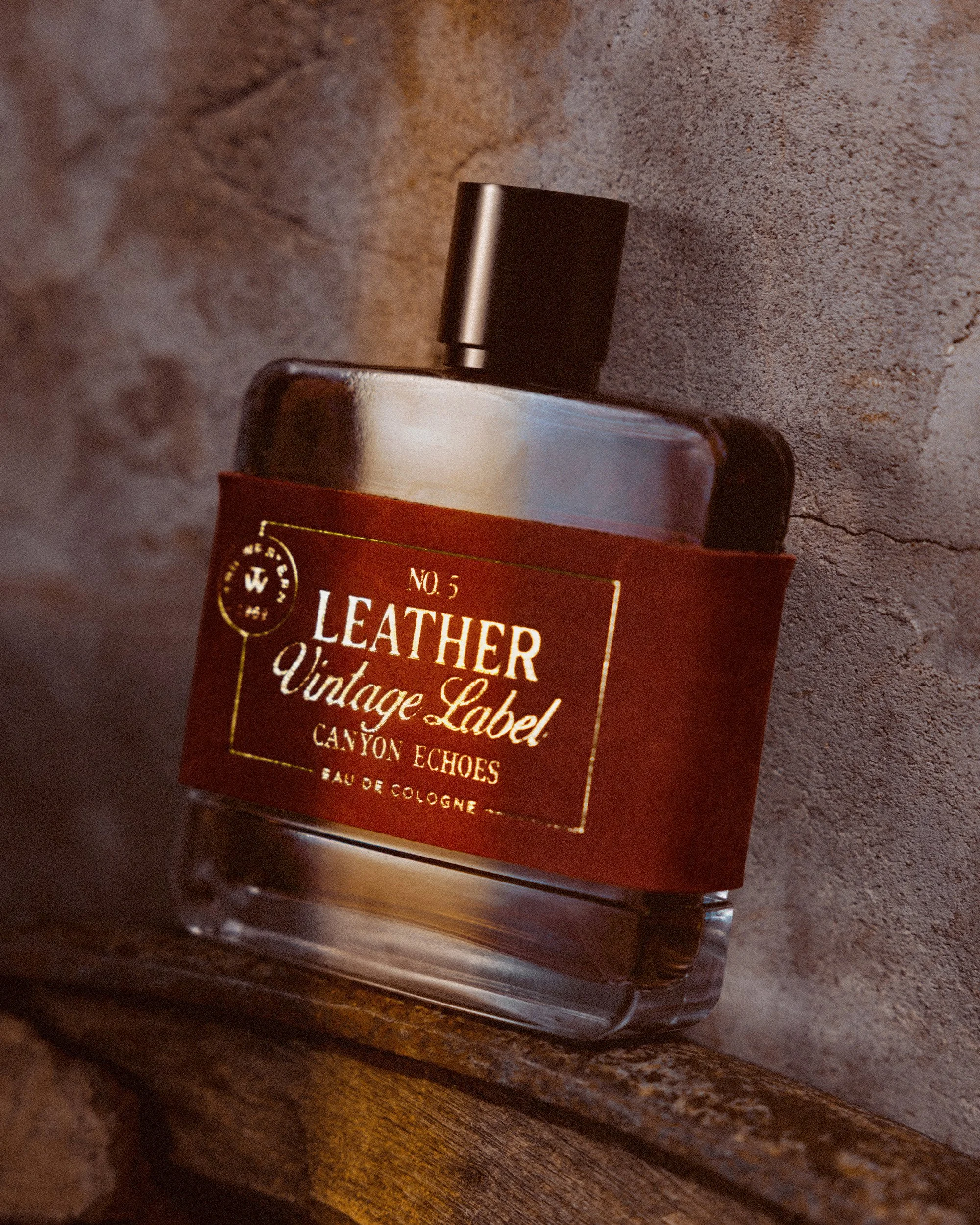 No. 5 Leather Vintage Label: Canyon Echoes tilted on a weathered ledge against an adobe wall, the label lit warm gold.