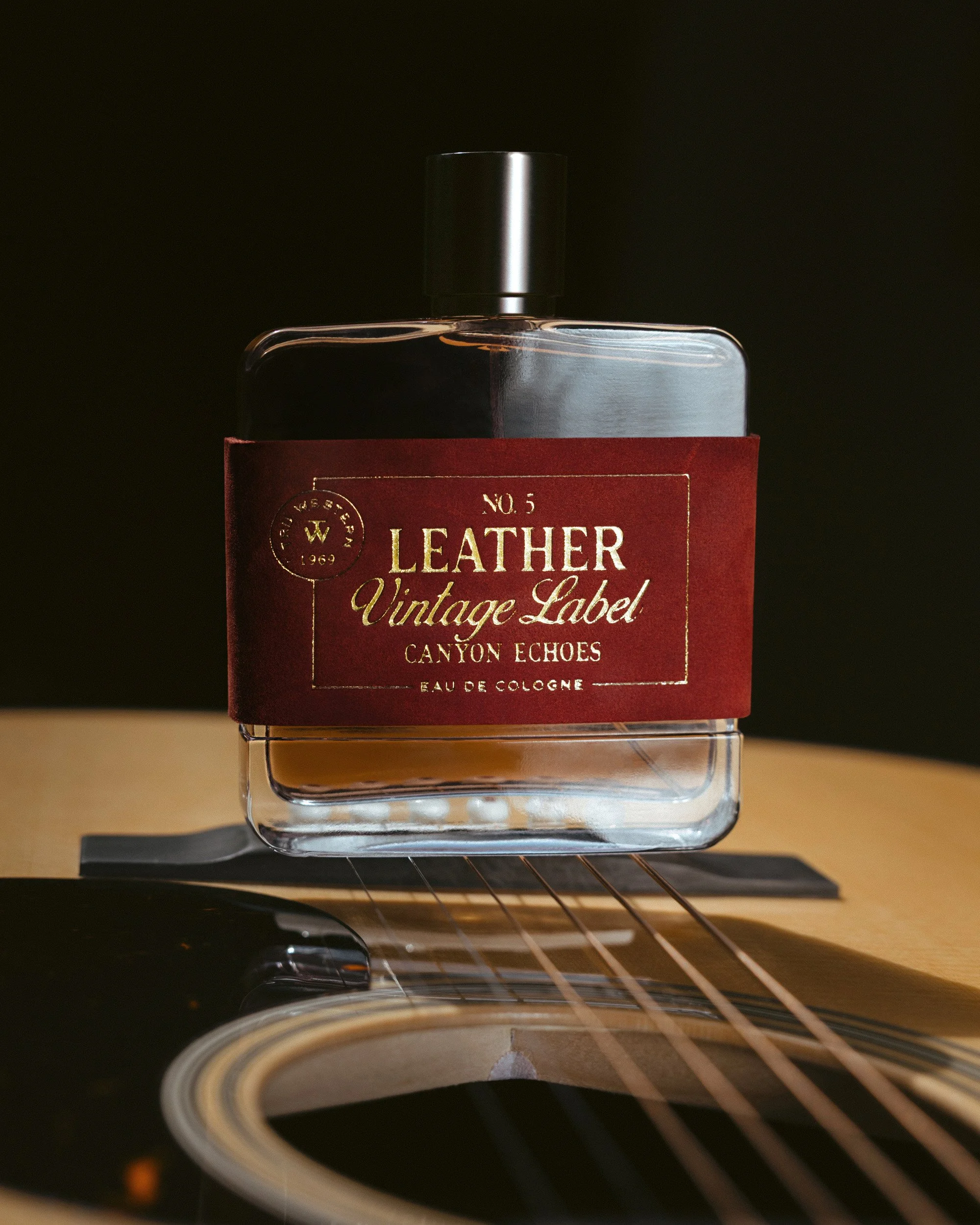 No. 5 Leather Vintage Label: Canyon Echoes resting on the strings of an acoustic guitar over the sound hole, black behind.