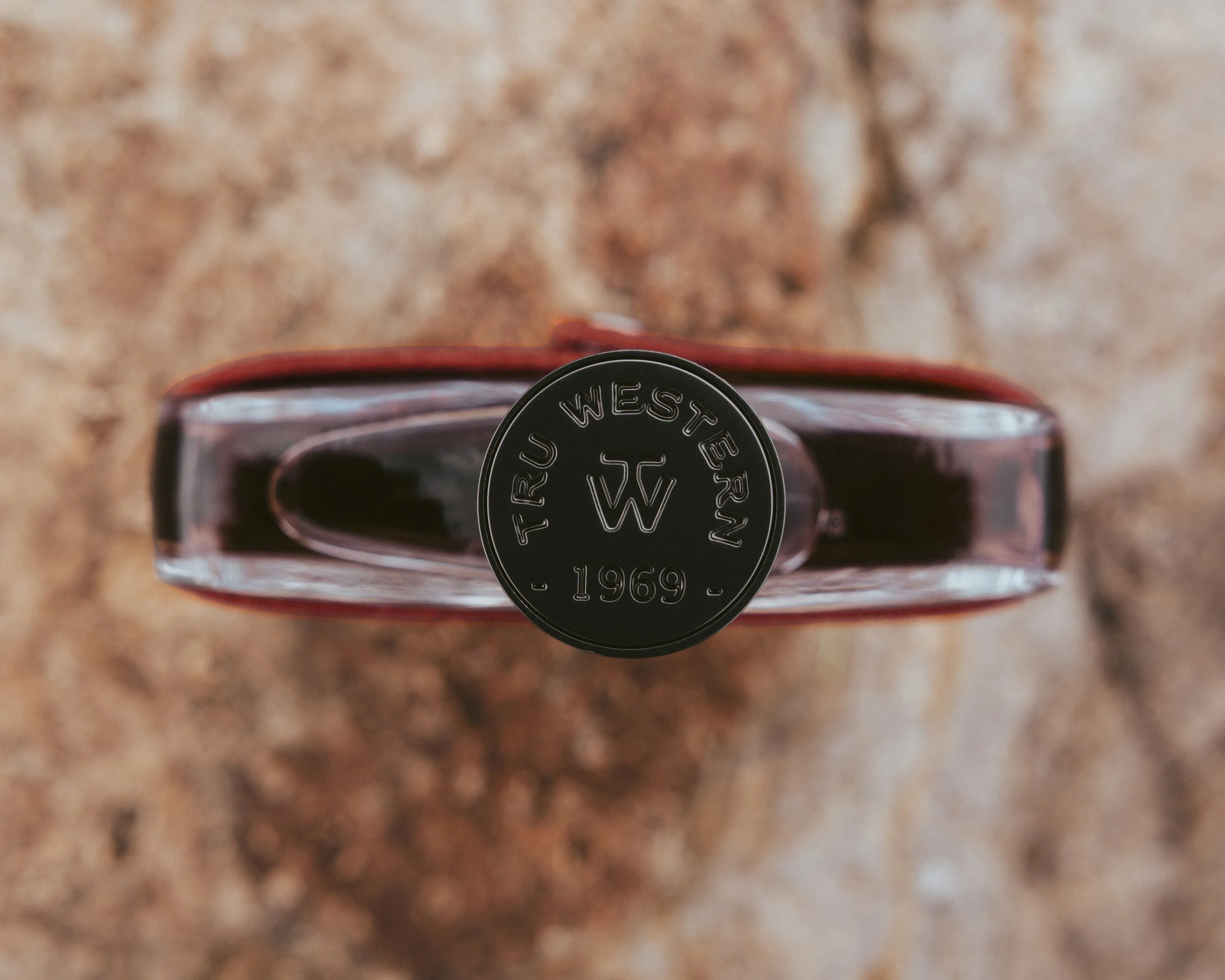 Looking straight down on the bottle cap stamped Tru Western 1969, the red suede label edge glowing against red desert rock.