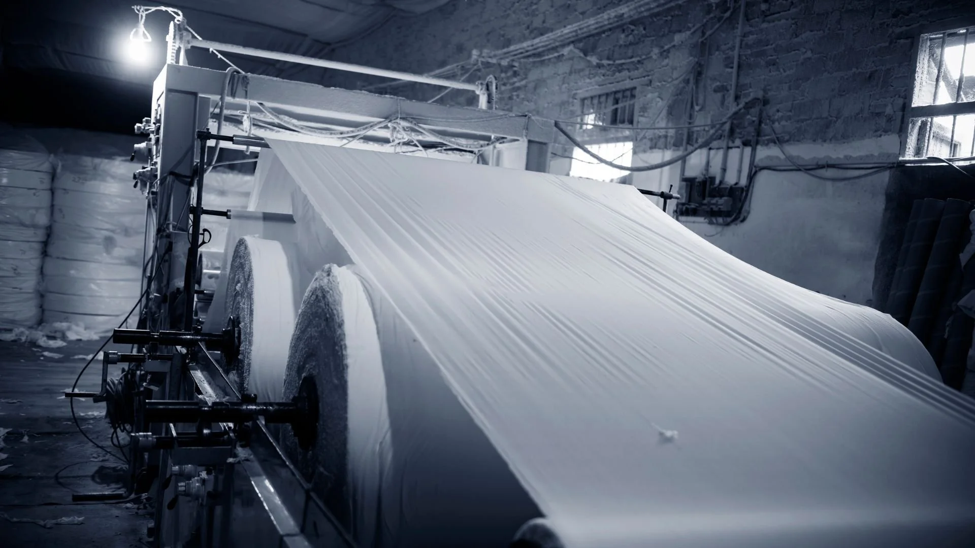 Industrial fabric manufacturing process with large rolls of fabric being fed through a machine in a factory setting.