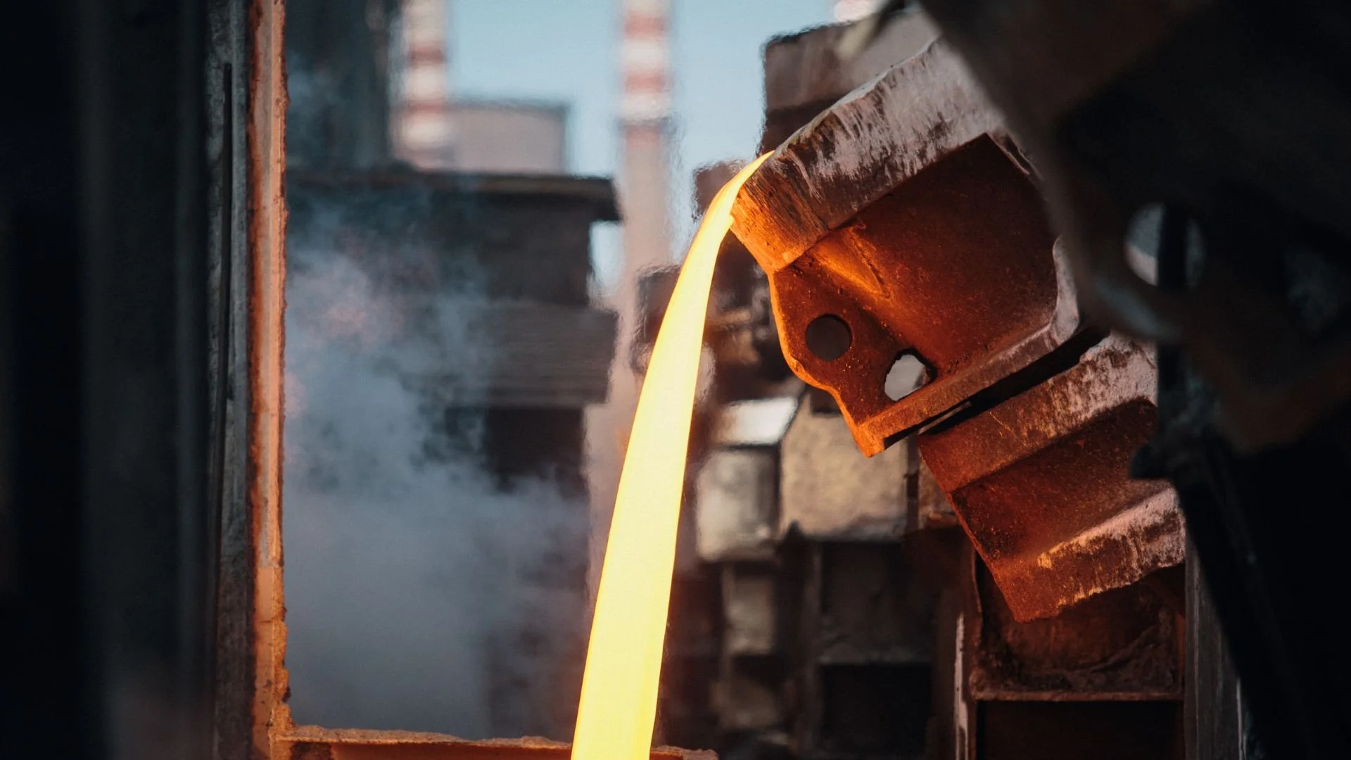 Molten metal flowing from a rusty metal pipe in an industrial setting.