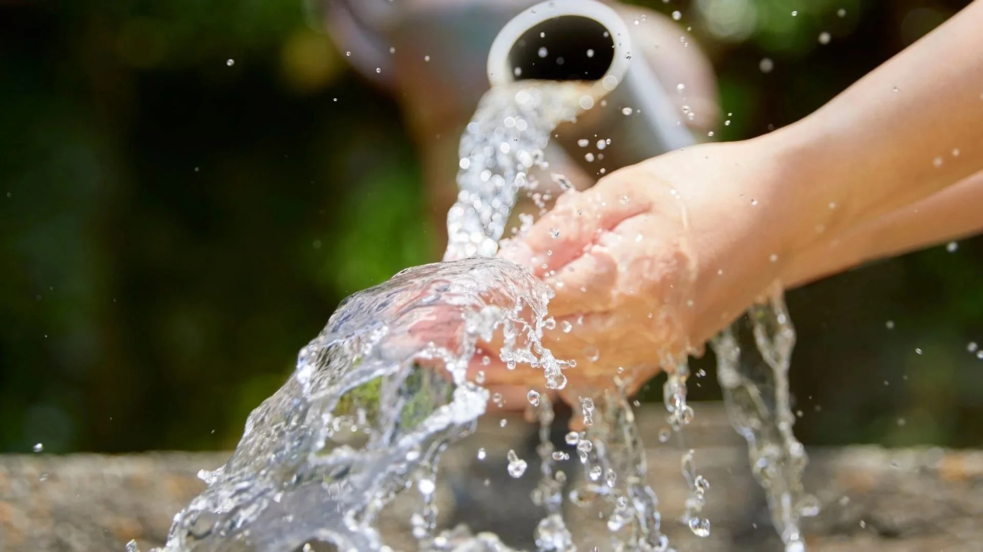 Person washing hands under running water from a faucet outdoors