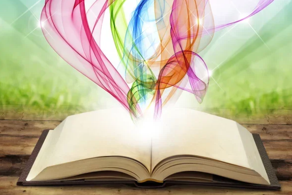 Open book on a wooden surface with colorful, flowing abstract smoke or light trails emerging from its pages, with a blurred green background.
