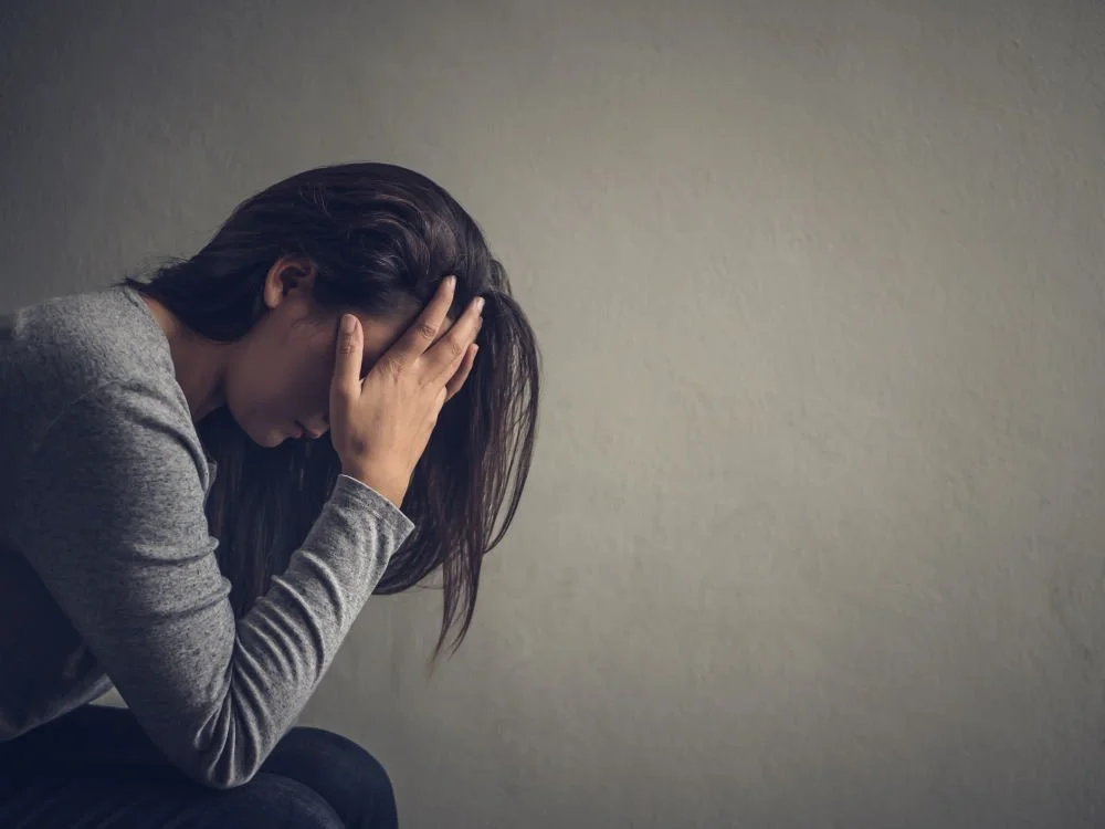 A woman sitting with her head down and hands on her forehead, appearing distressed or upset.