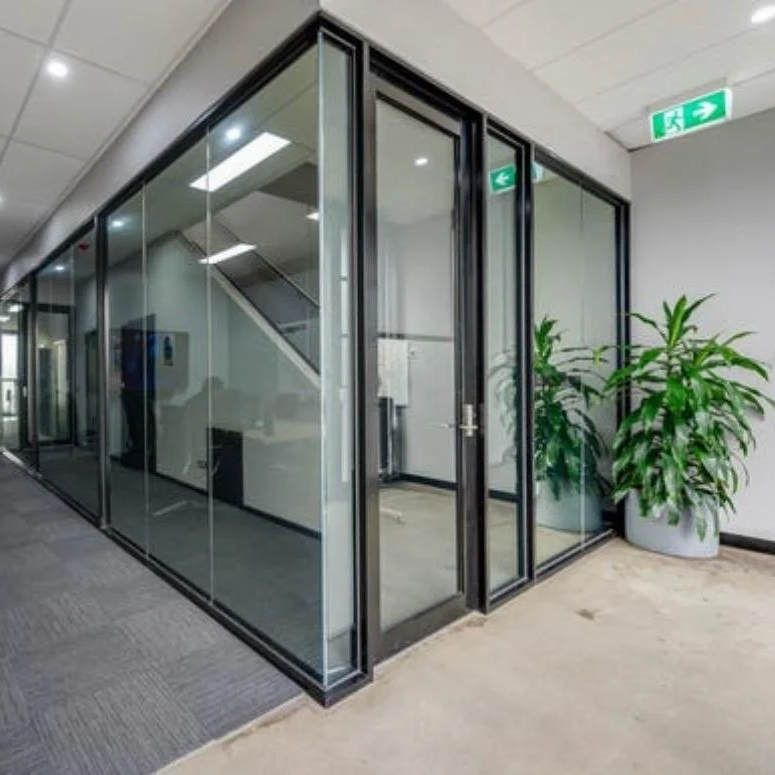 Glass office with black framing, a green plant in a white pot, and an emergency exit sign on the ceiling.