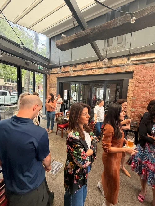 People socializing in a brewery or pub with exposed brick walls and large glass windows.