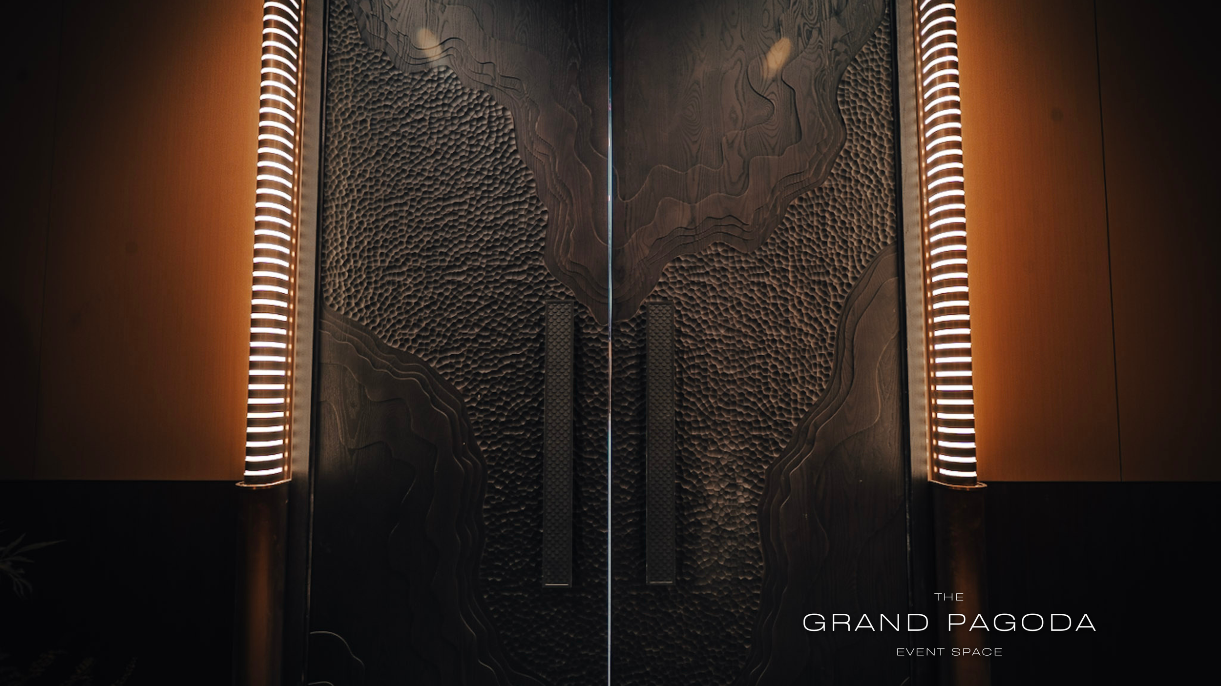 Double doors with textured, layered black wood design and illuminated vertical light strips on each side. Text at the bottom right reads 'The Grand Págoda Event Space'.