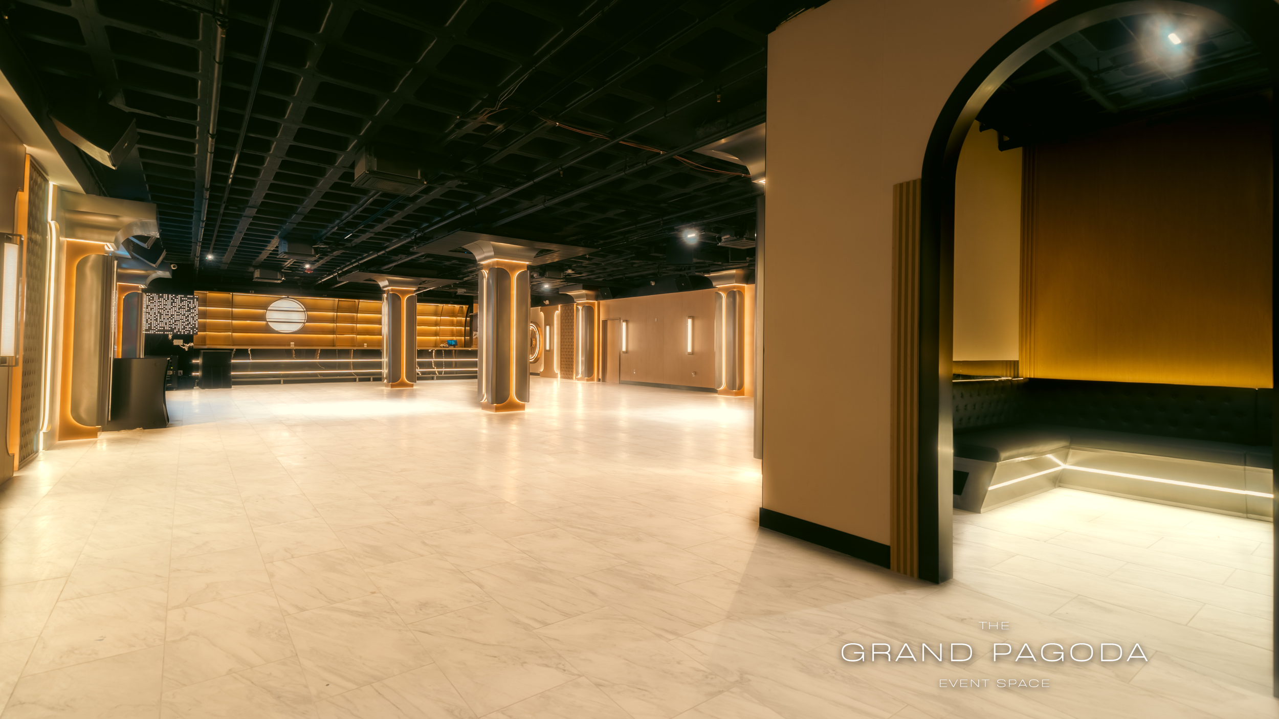 Modern event space with illuminated columns, sleek black ceiling, and warm lighting accents. The polished floor with minimal decor suggests an upscale venue named 'The Grand Pagoda'.