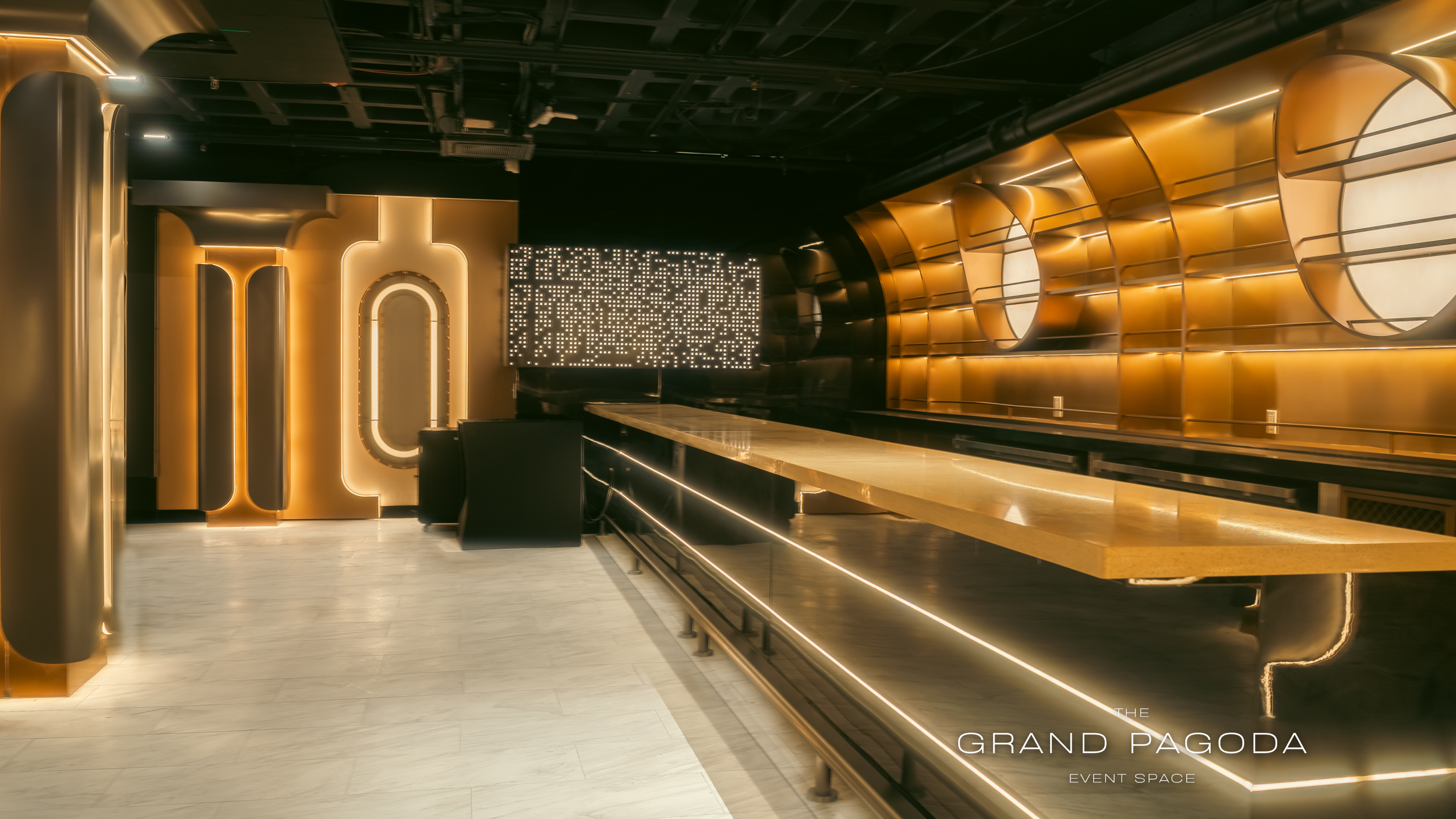 Interior view of a modern event space with black ceiling, illuminated gold accents, a large illuminated sign, and a marble-topped bar counter.