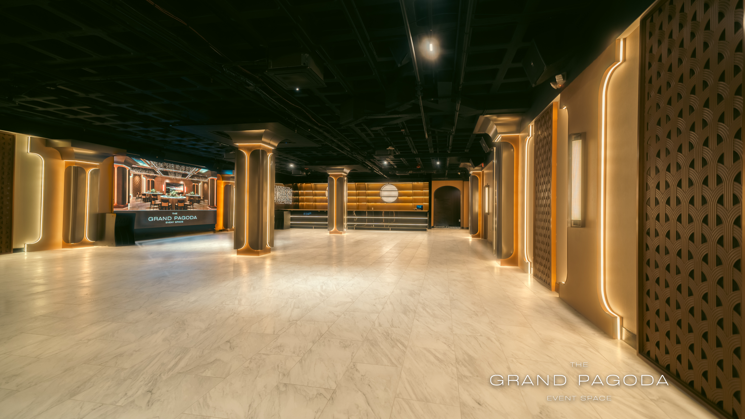 Empty event space with modern interior design, illuminated golden and beige accents, and a large LED screen displaying 'The Grand Pagoda.'