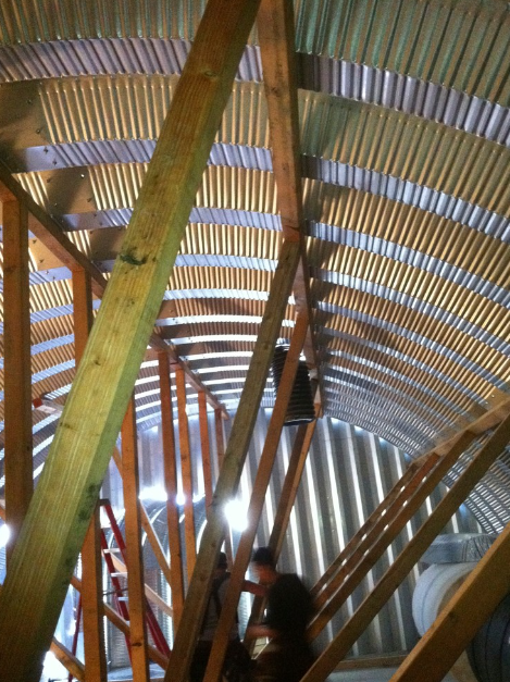 View inside a wooden and metal structure under construction, with scaffolding and a ladder visible.