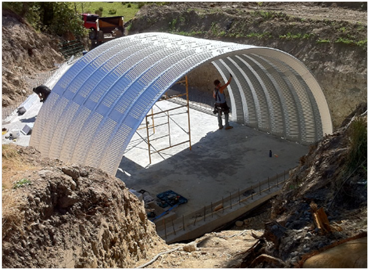 Construction site with a partially built metal tunnel structure, workers present, and construction tools on the ground.