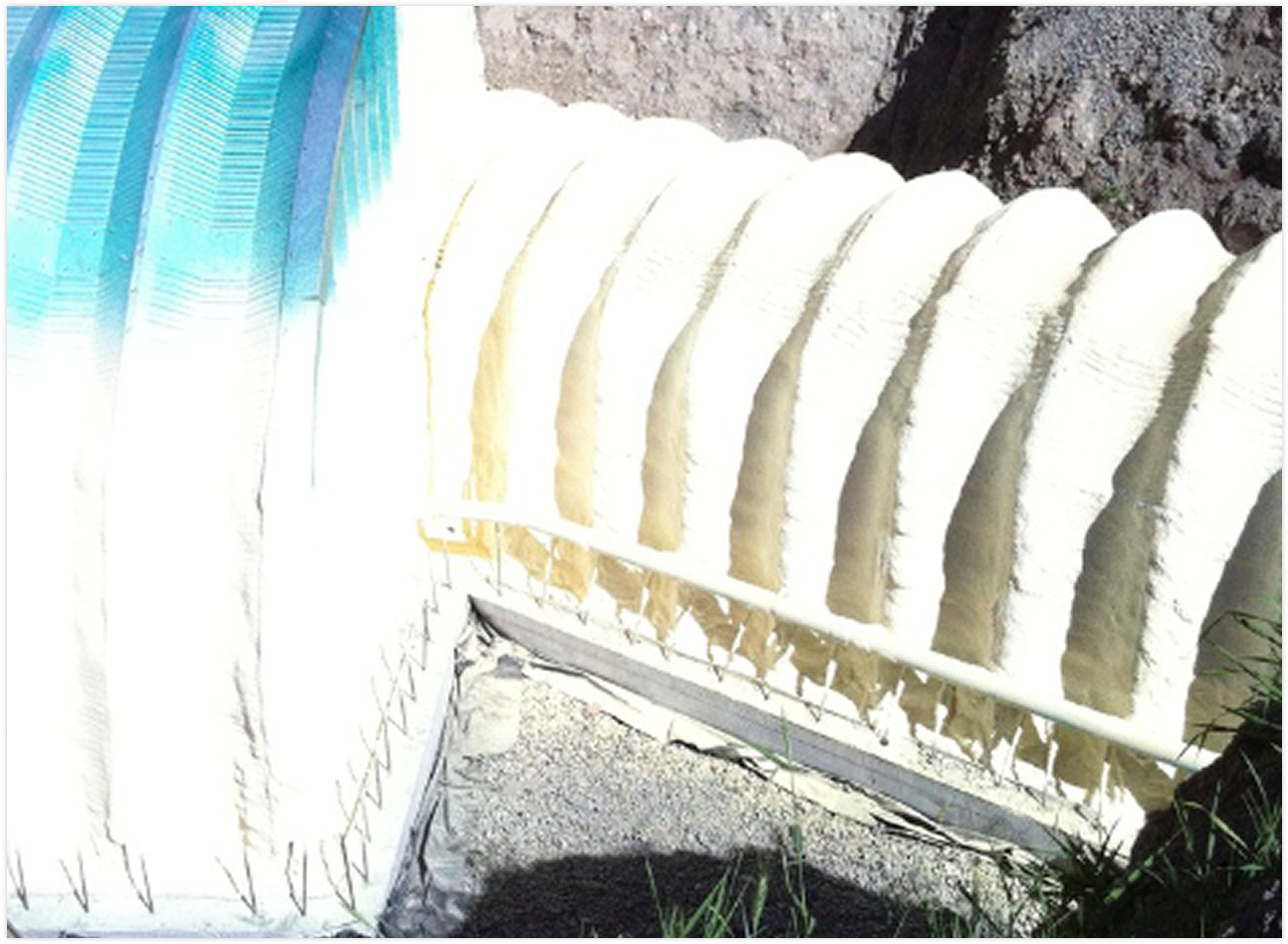 A dam with water flowing over it, accompanied by a blue and white striped cloth or tarp on the left side, and some greenery at the bottom right corner.
