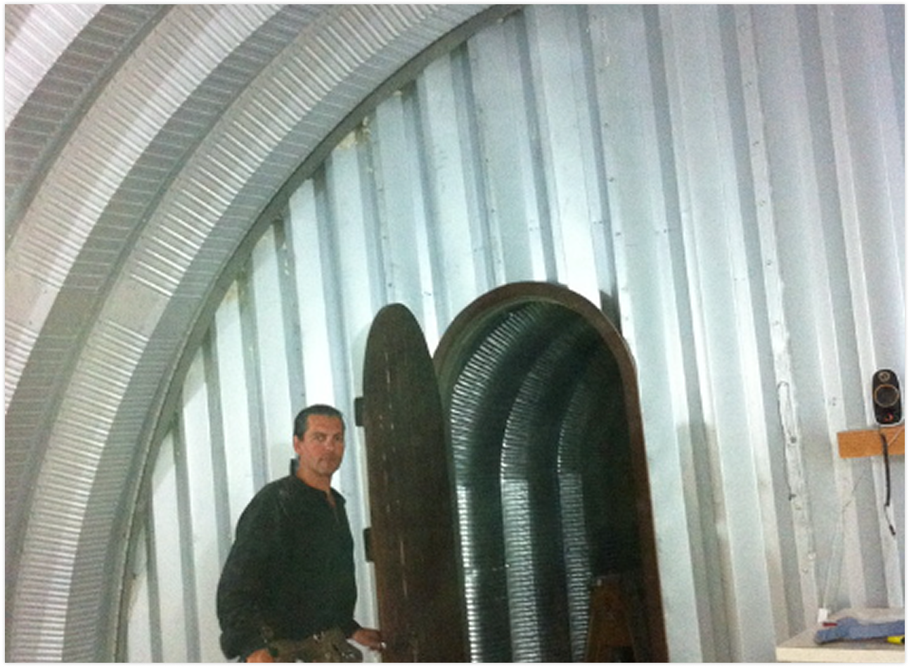 A man standing inside a building under construction with metal framing walls and an arched doorway.