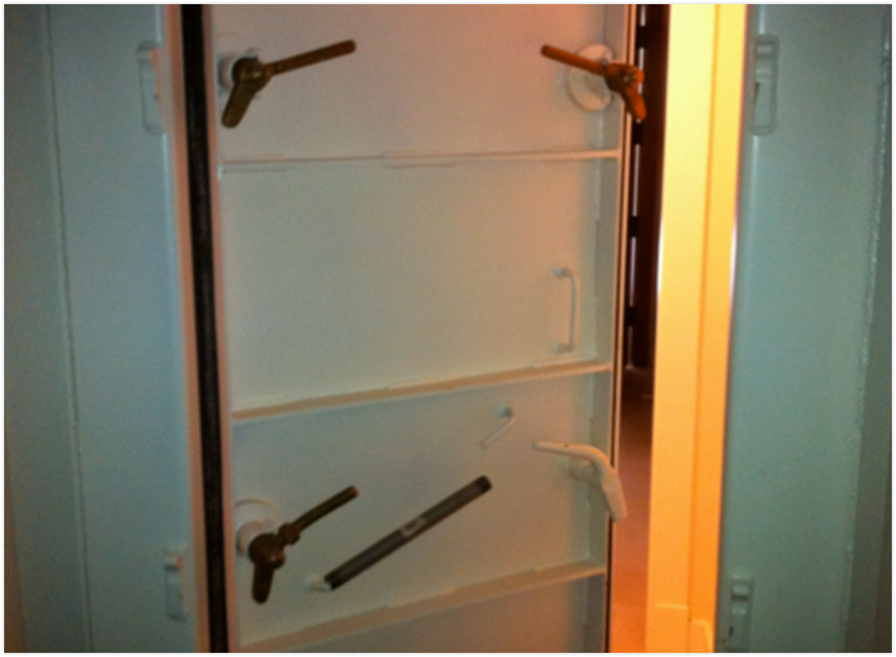 Interior of a large metal safe door with multiple locking mechanisms and handles, open and showing the inside of the safe.