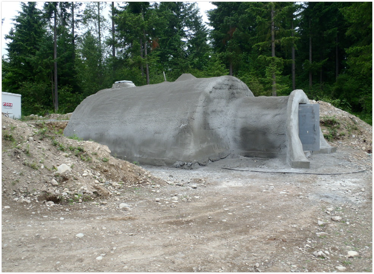 Large concrete structure resembling a submarine partially buried in the ground at a construction site, with trees in the background.