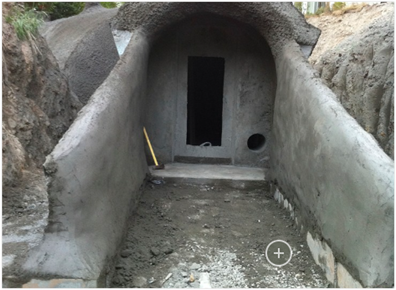 Concrete tunnel opening under construction with dirt ground and construction tools inside.