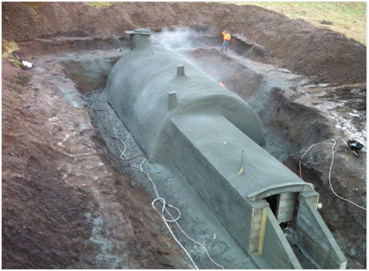 A large concrete underground tunnel or vault being constructed in a deep excavation site, with a worker standing nearby.