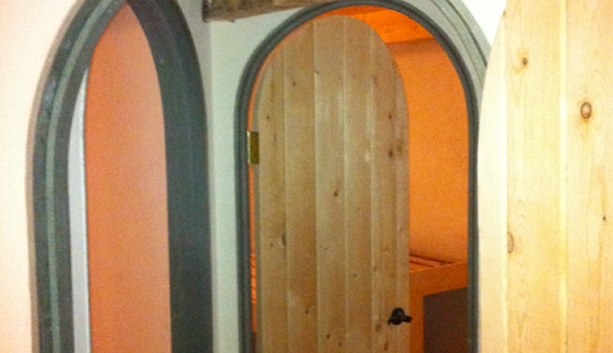 An interior view of a doorway with an arched top, revealing a small room with wooden walls and a door handle.