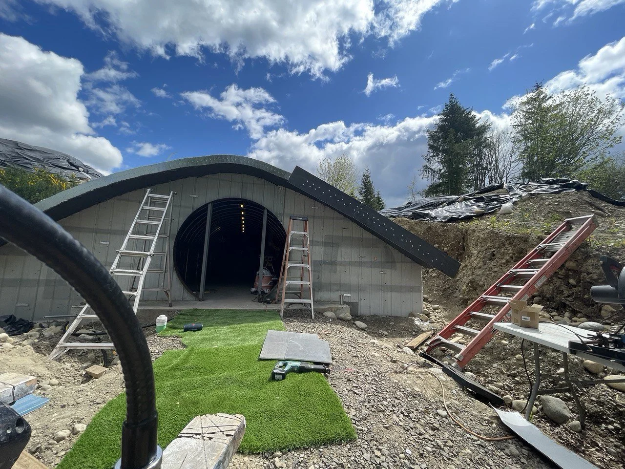 Under construction of a dome-shaped structure with ladders, tools, and construction materials outside on a partly cloudy day.