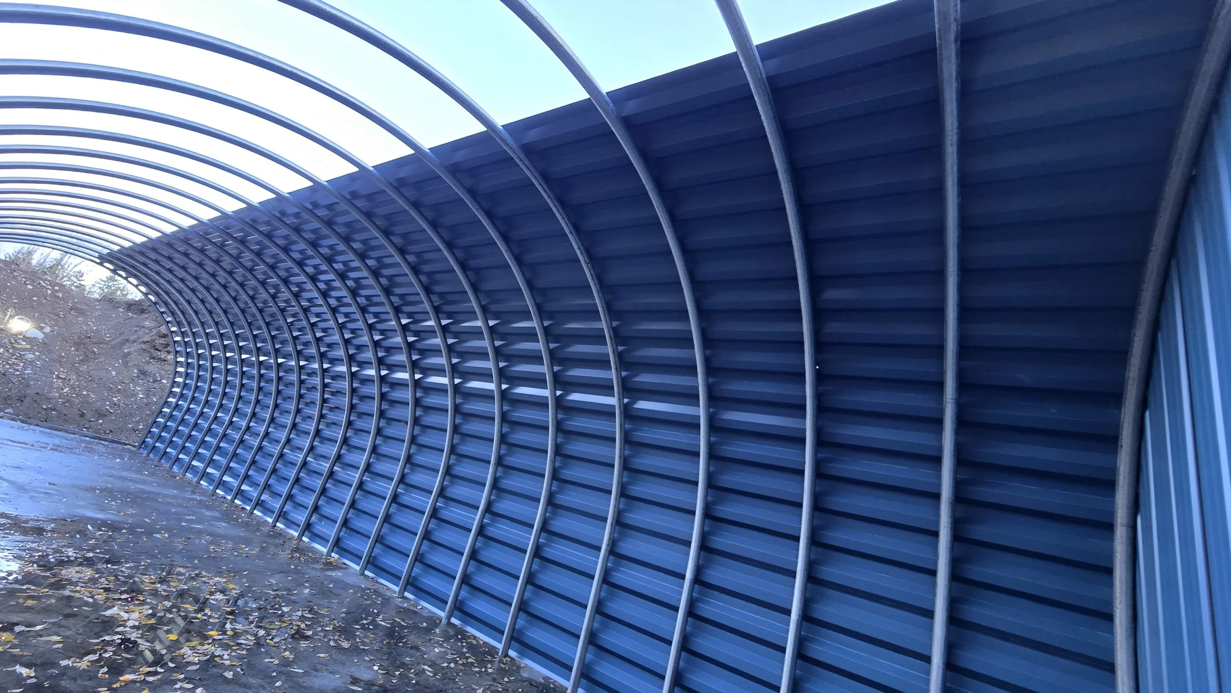 Constructed blue metal tunnel with curved ribs, positioned outdoors on a damp, leaf-covered ground.