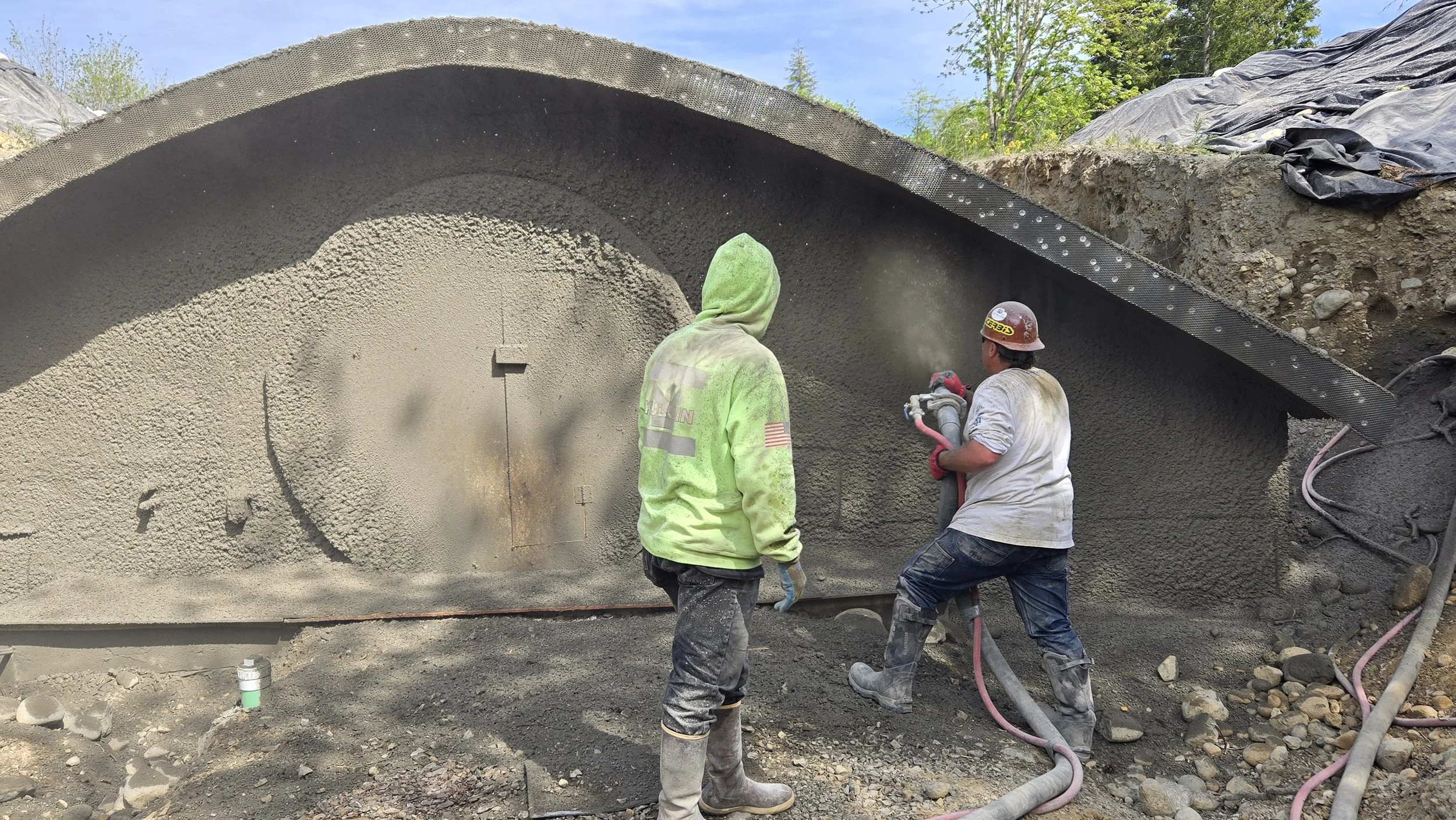 Two construction workers pounding concrete on a tunnel wall at a construction site.