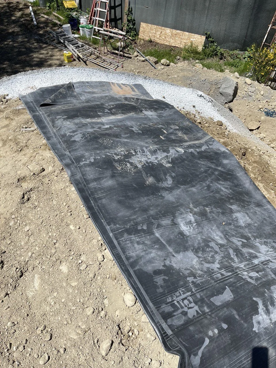 Construction site with black tarp, gravel, and various tools and materials