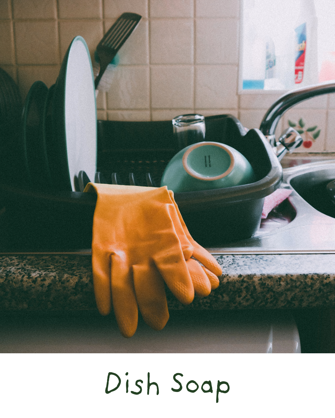 A kitchen sink filled with dishes, including a dish drying rack, clean plates, a bowl, and a glass. An orange rubber glove is hanging over the edge of the sink. The background shows a tiled wall and a window with some decorative items.