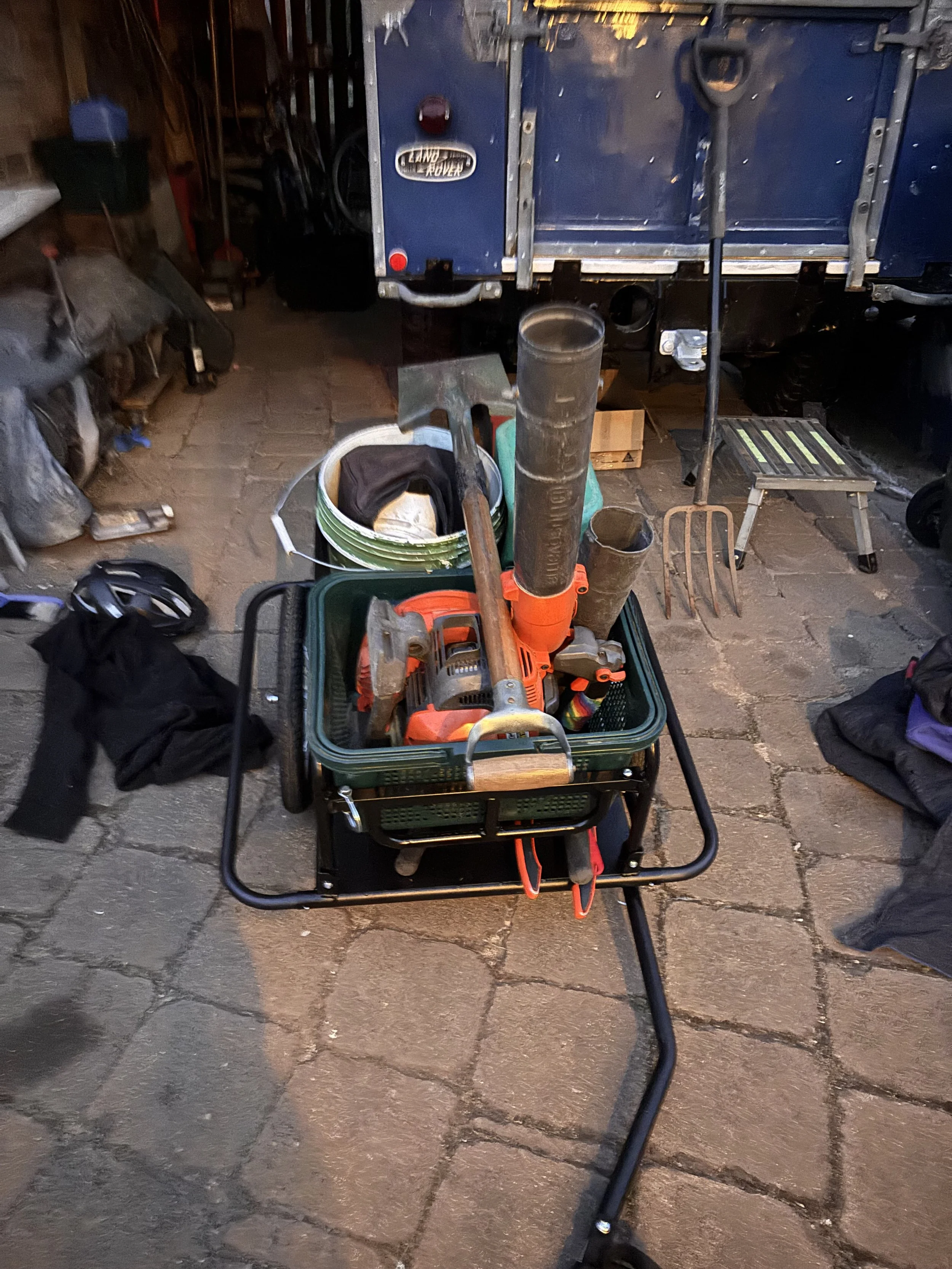 A workbench with various tools and equipment, including a leaf blower, drill, and pipes, in a garage or workshop setting.
