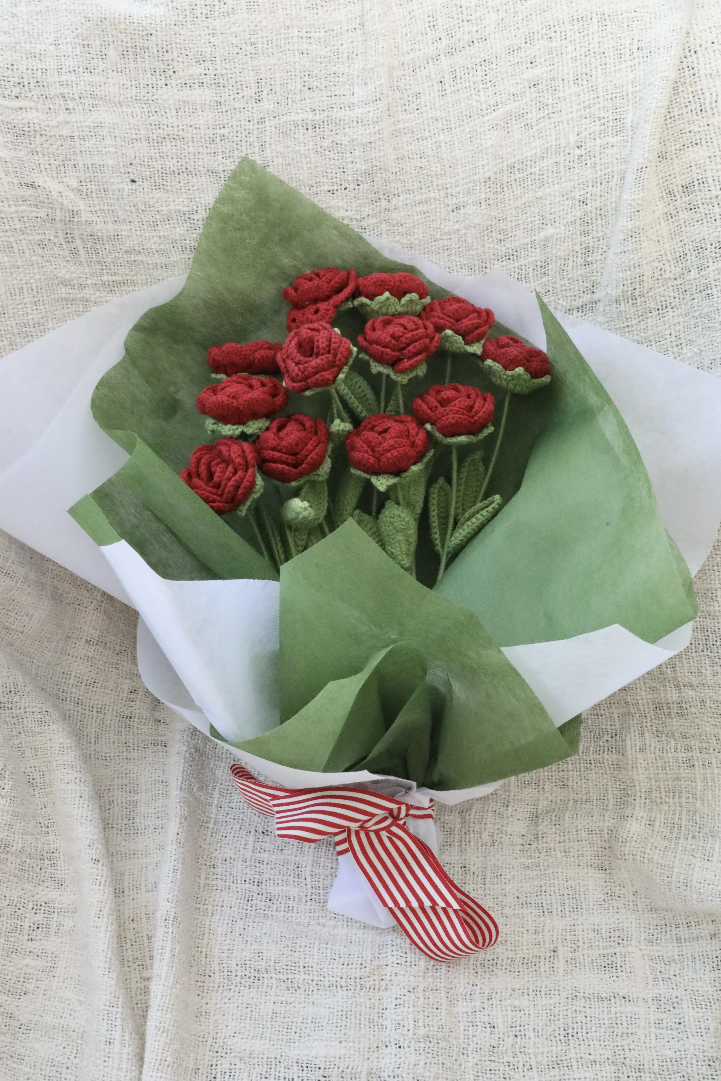A bouquet of red knitted roses wrapped in green paper with a red and white striped bow.