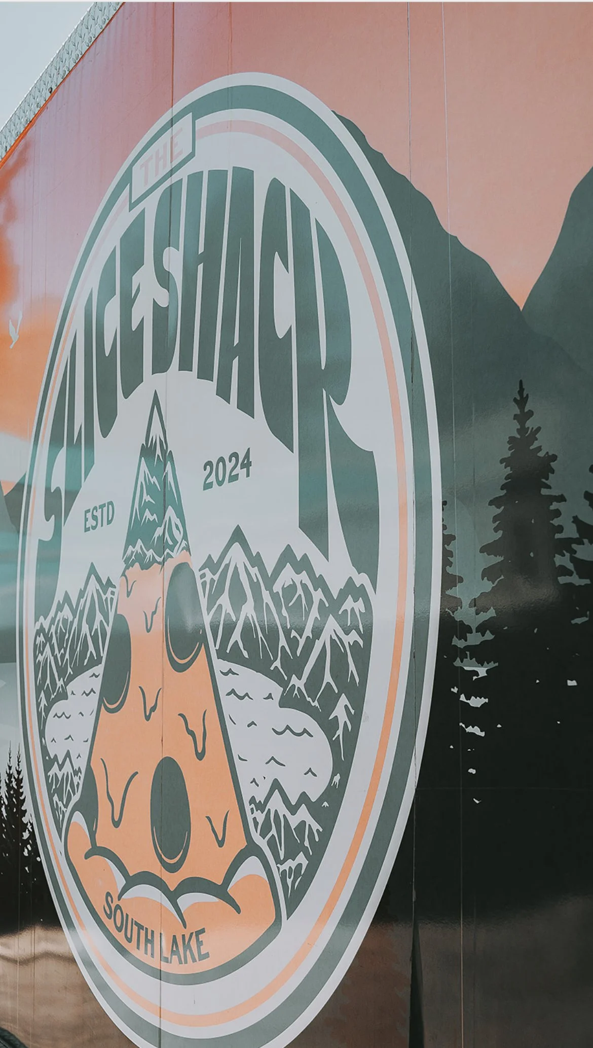A circular logo with mountains, a lake, and a bear skull in the center. Text around the logo reads 'The Fresh Hach 2024 ESTD South Lake' with a mountain and trees in the background.