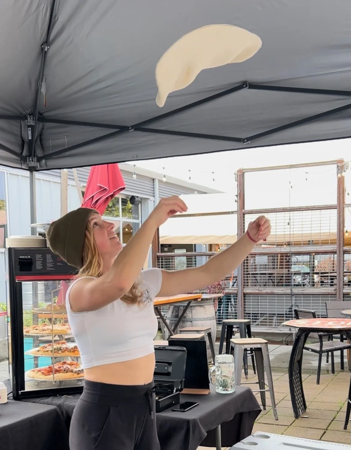 A woman tossing a slice of pizza in the air at an outdoor dining area.