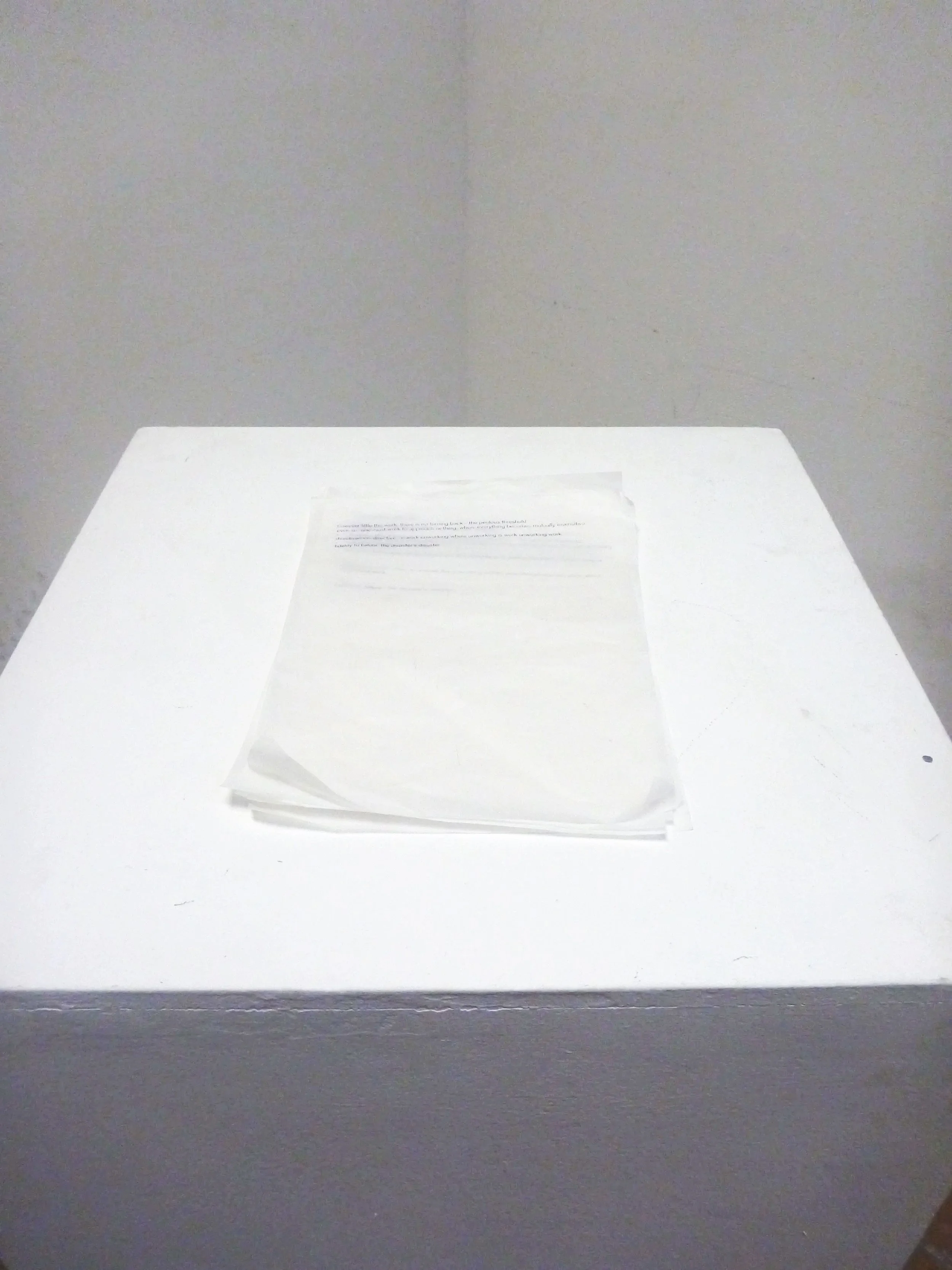 A white table with a stack of papers on it, against a plain wall.