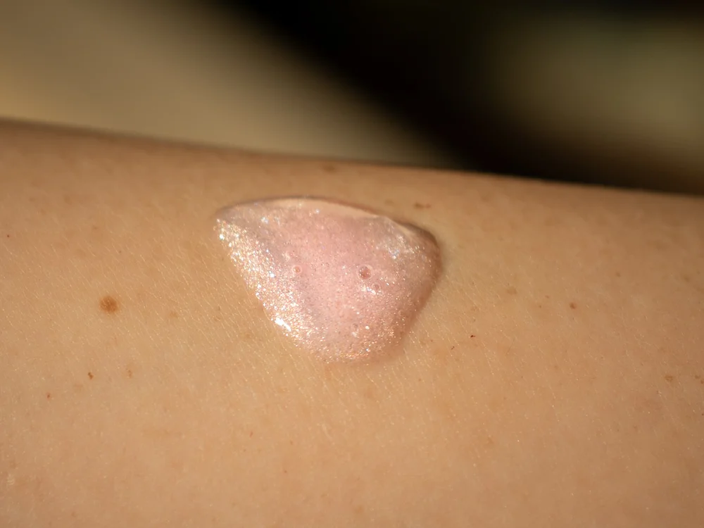 A swatch of pink shimmer body oil on skin before it is worked in