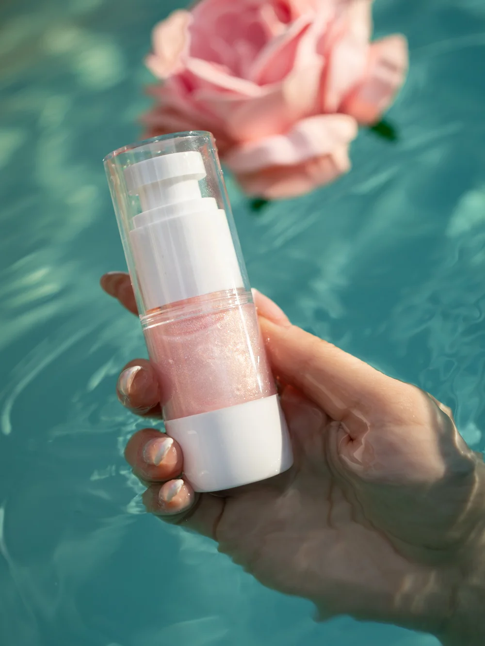A hand holding the Bug Babe bottle above teal pool water, showing the milky pink oil inside