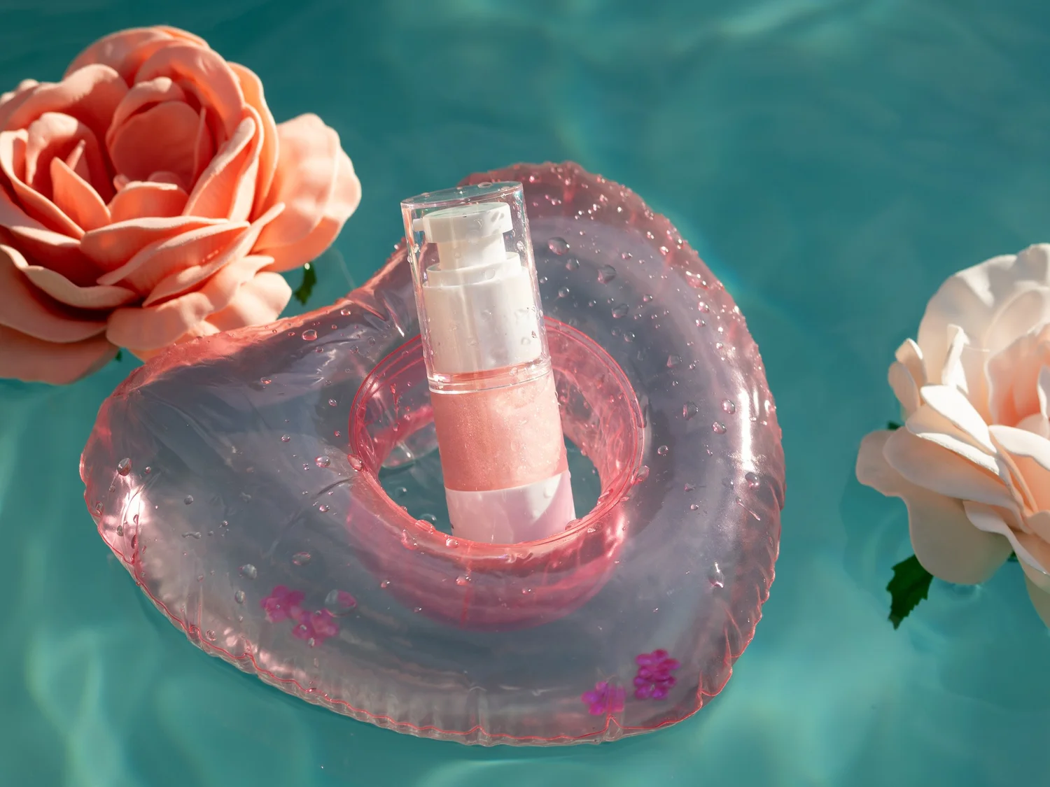 The Bug Babe bottle resting in a pink flower pool float on turquoise water, surrounded by peach roses