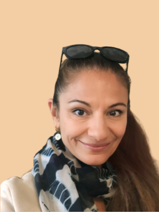 A woman with sunglasses on her head, wearing earrings and a patterned scarf, smiling at the camera against a beige background.